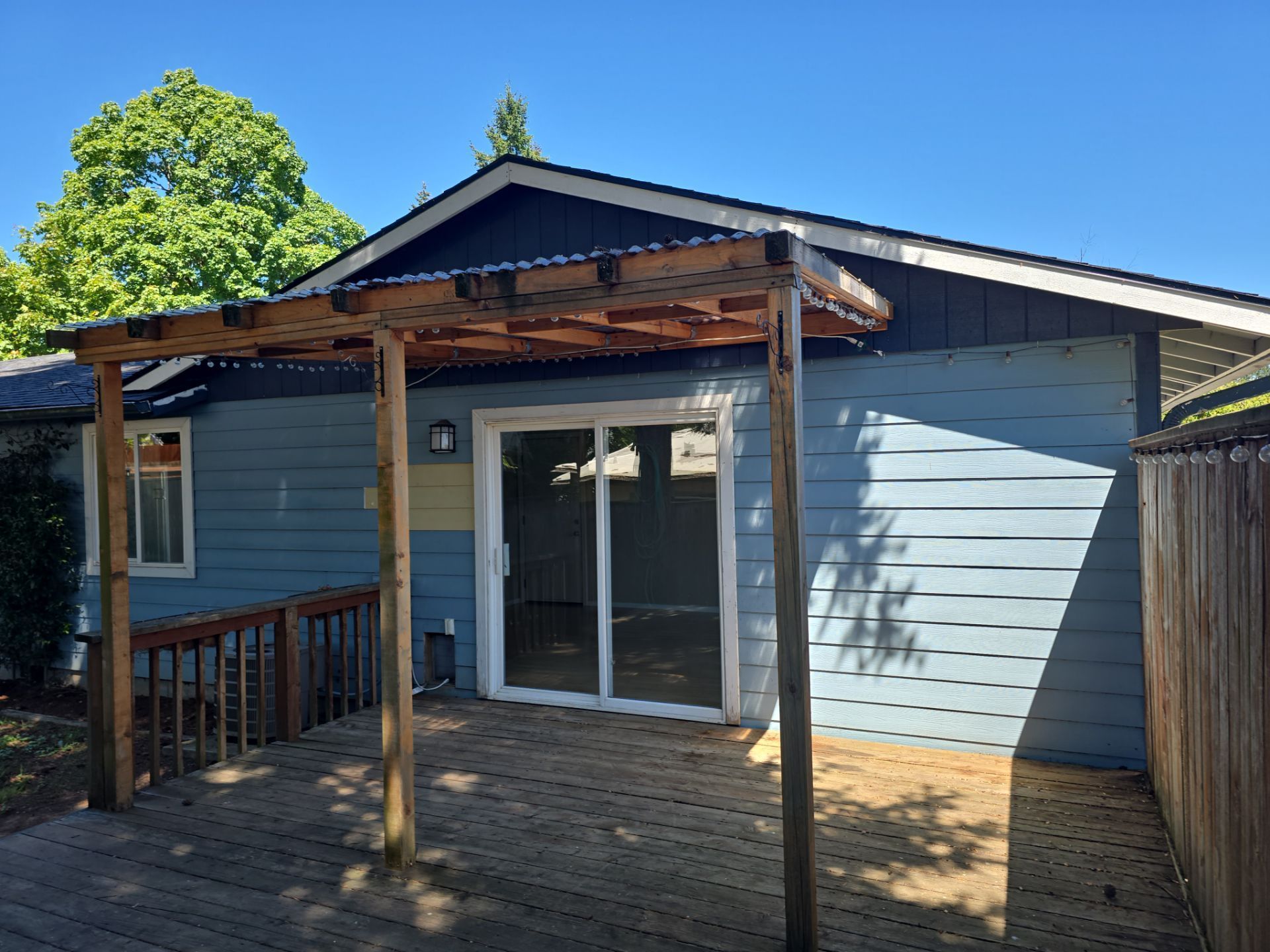 Blue house porch with sliding glass doors, wooden deck, and pergola under a clear sky