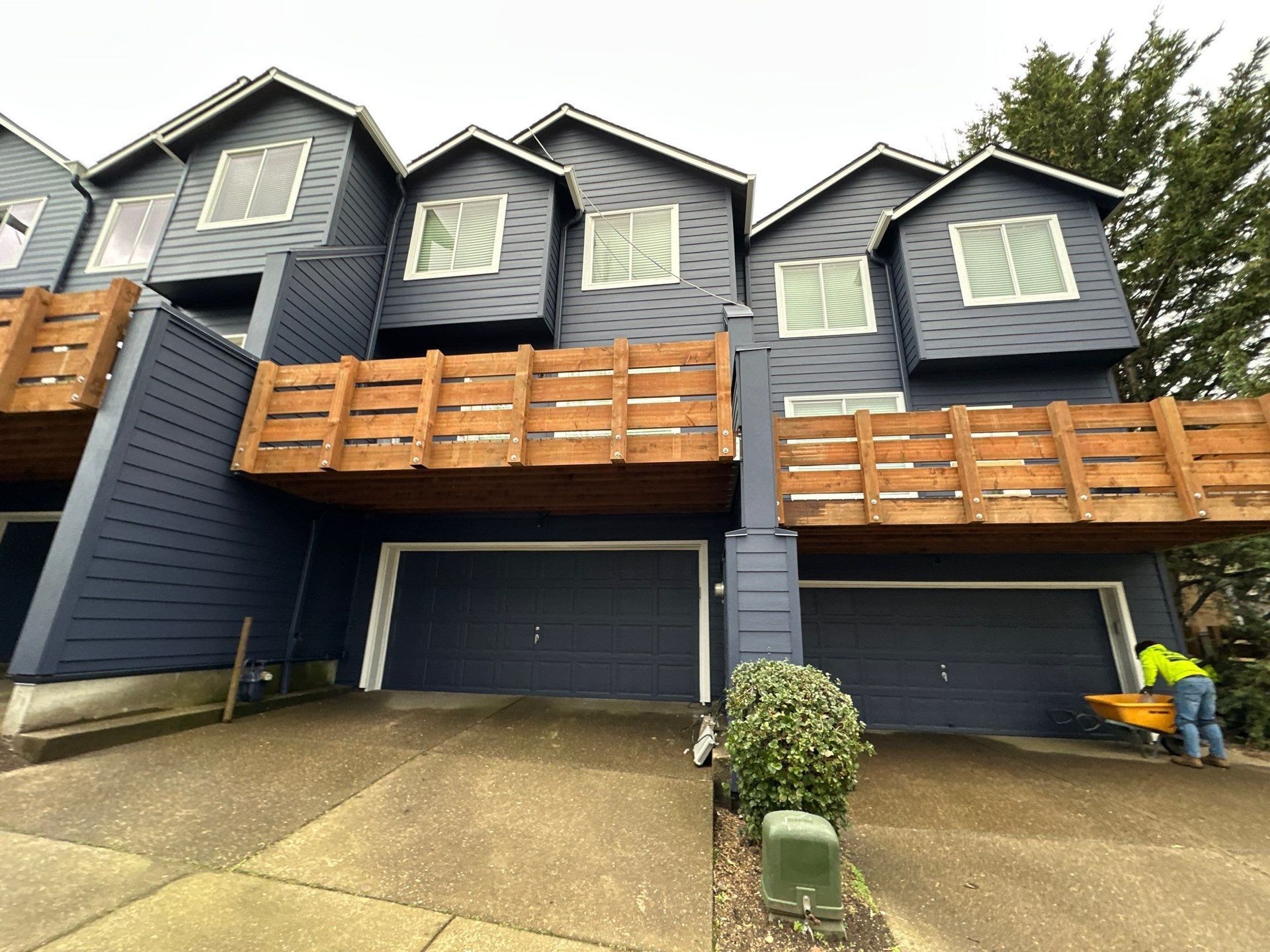 Blue townhouse with wooden balconies and two garages, viewed from a sloped driveway
