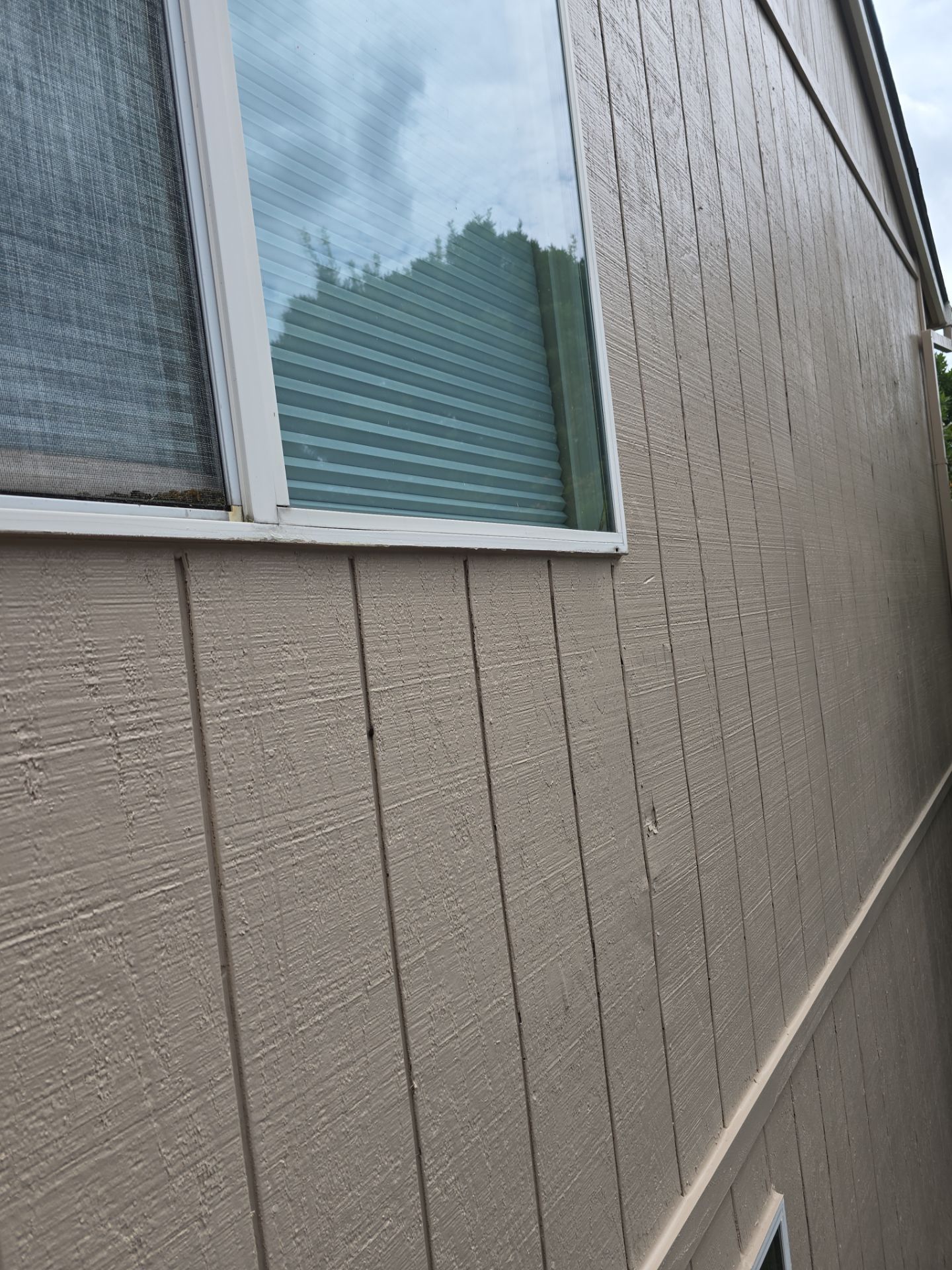Close-up of a beige building wall with a window and white trim along a narrow side alley
