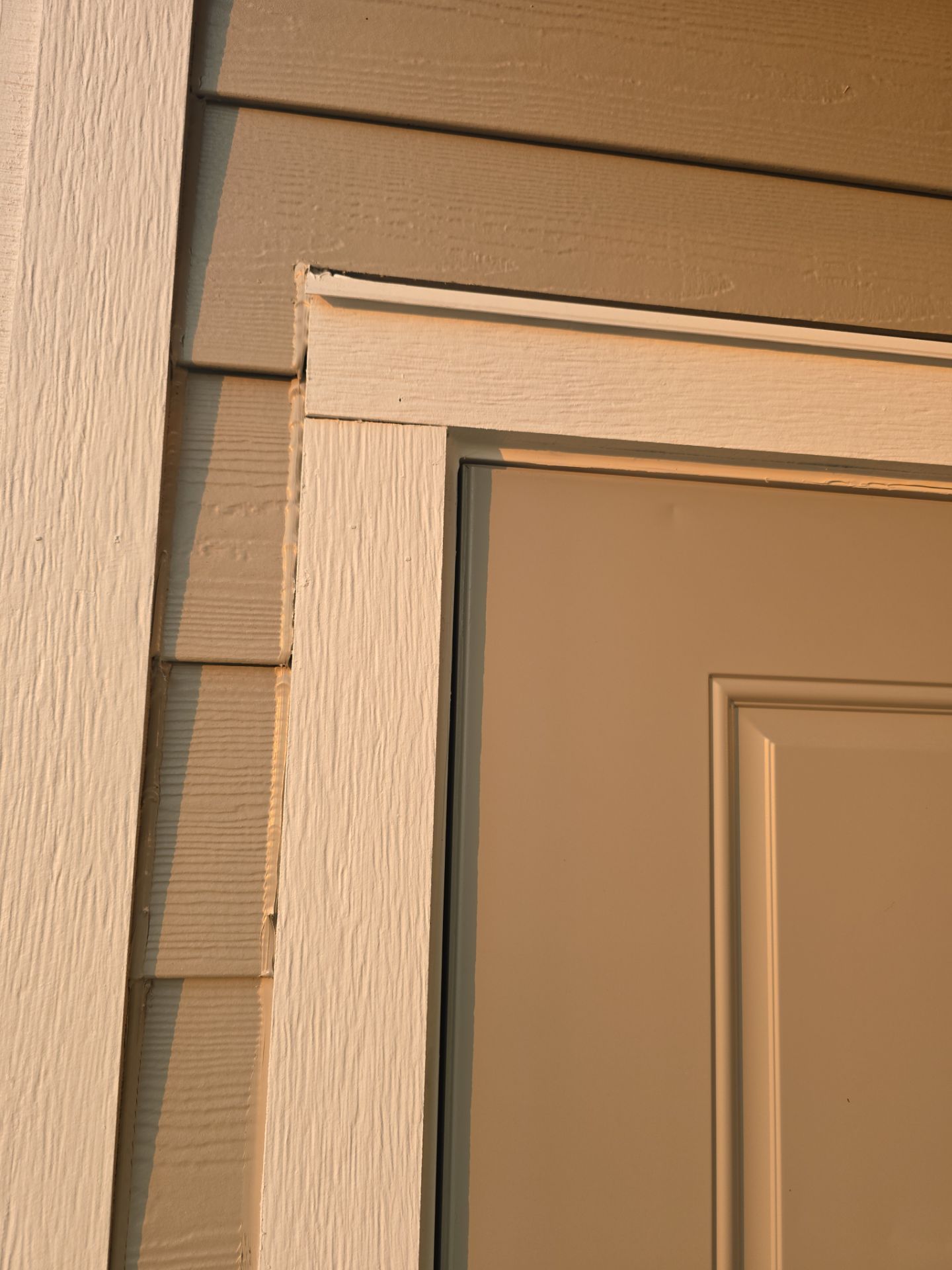 Close-up of tan house trim and siding around a beige door frame