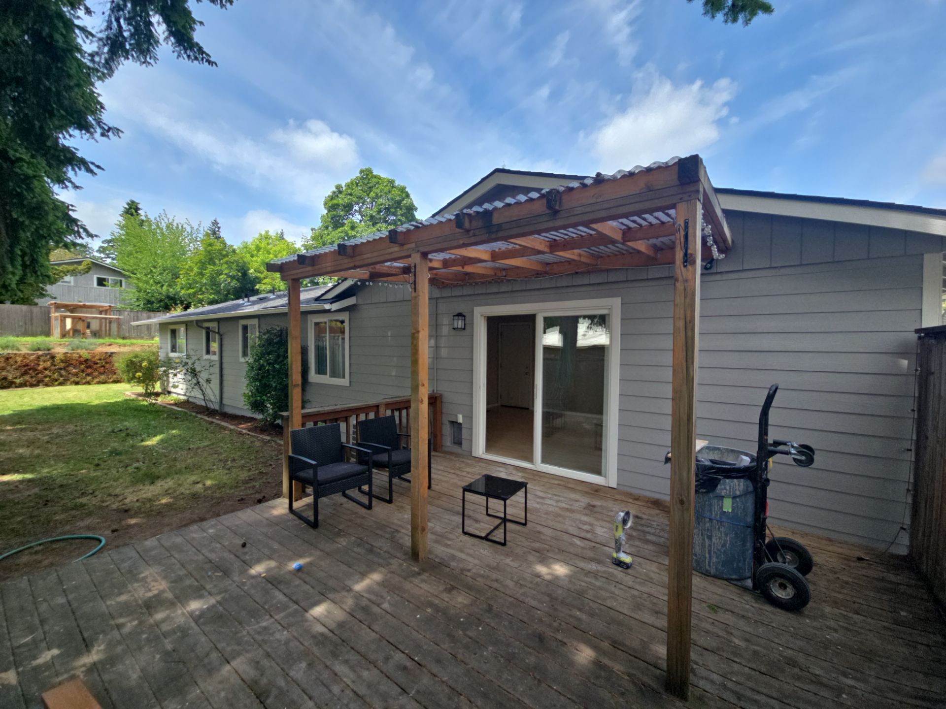Backyard patio with pergola, sliding door, bench, and gray house exterior under a blue sky