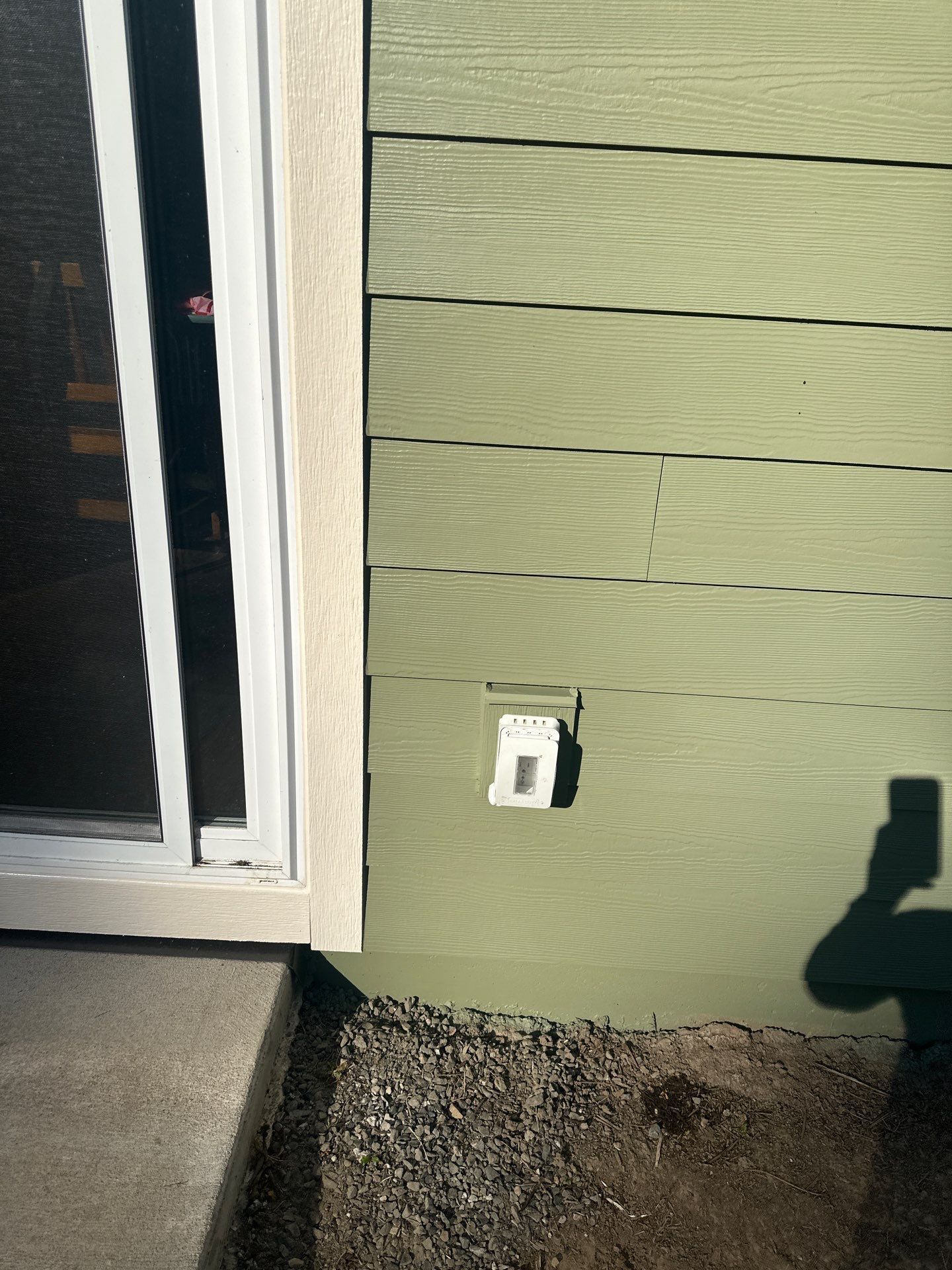 Exterior wall with green siding, a door edge, and a small white outlet near the ground.