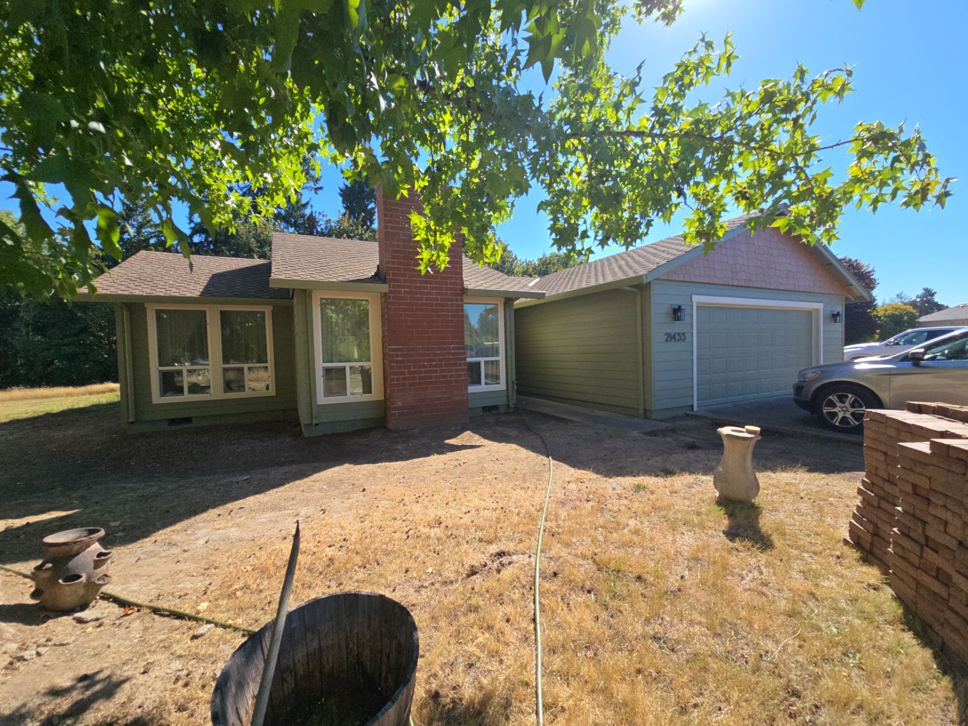 Single-story brick house with a garage, front yard, and large tree in bright daylight