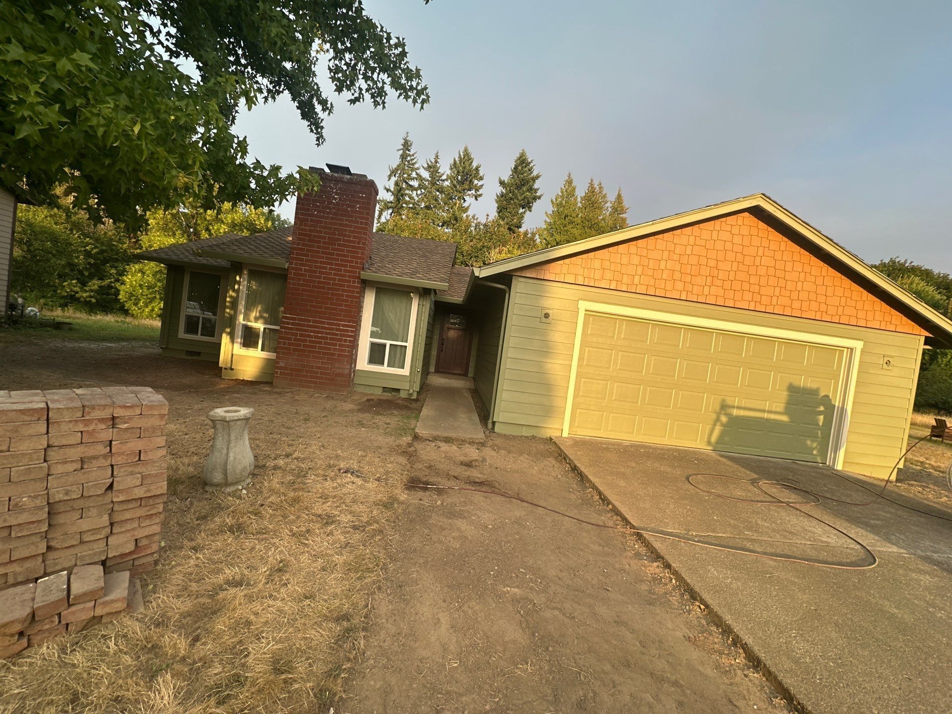 Suburban house with brick chimney, orange garage, and driveway in a wooded yard