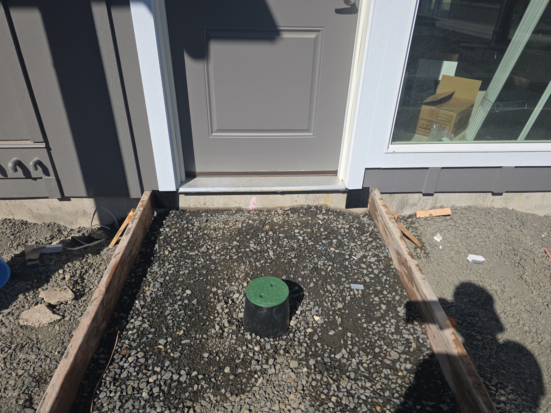 Front entry walkway with a green-capped pipe centered in gravel beside a house door and window.