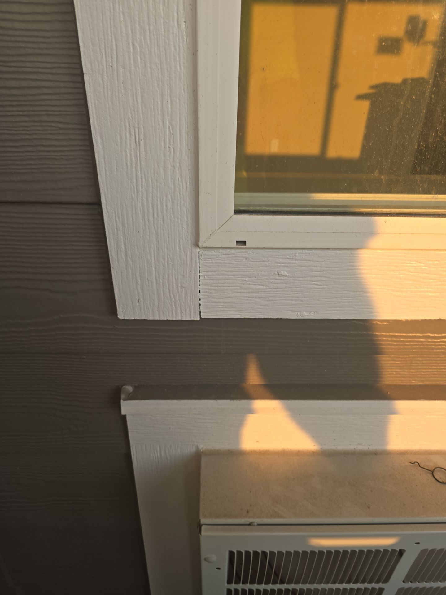Exterior wall and window with gray siding, white trim, and sunlight casting shadows.