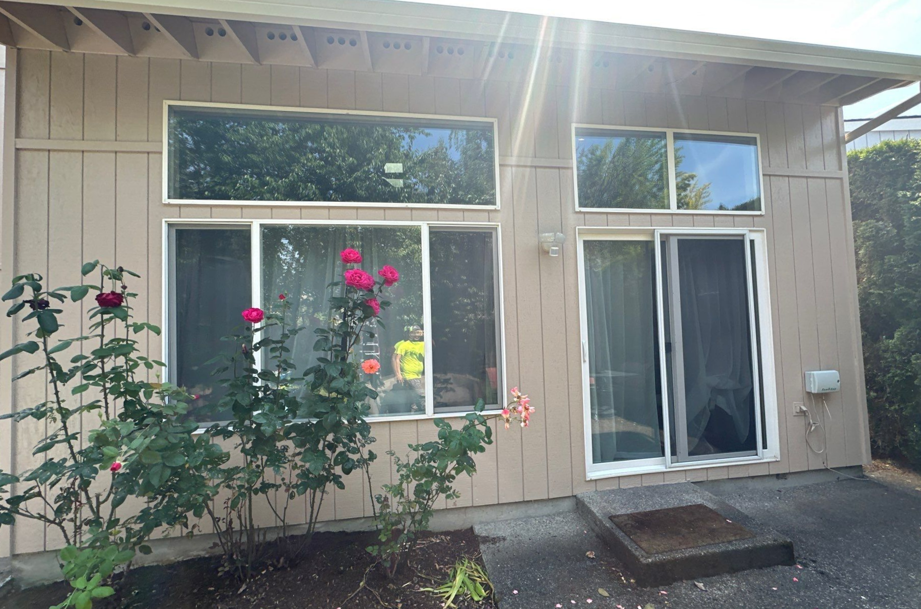 Front of a beige house with windows, a glass door, and pink flowers in the yard