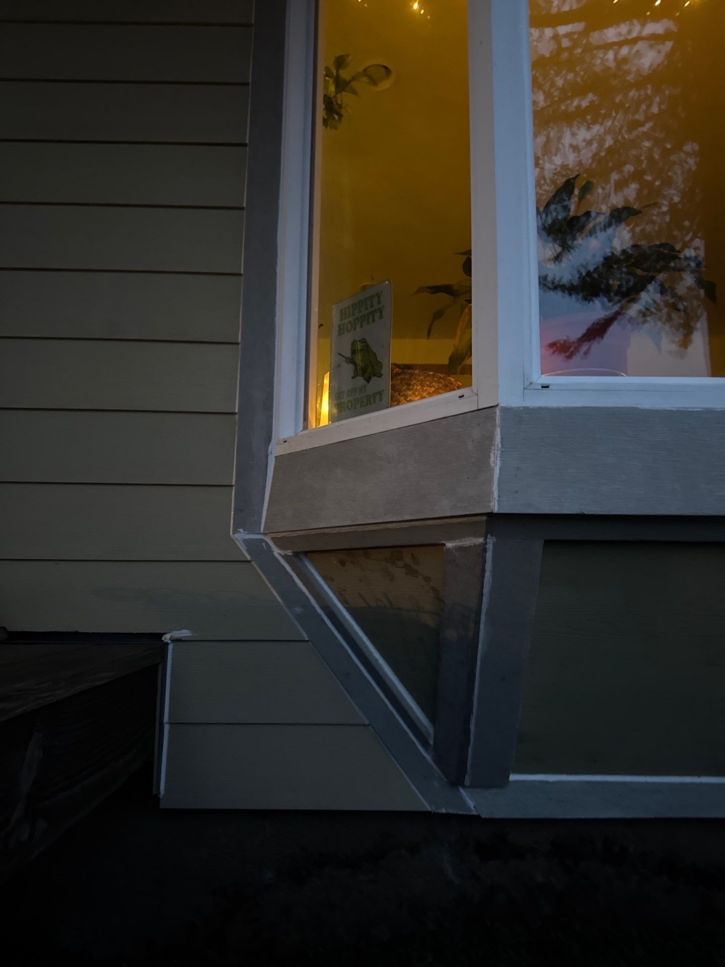 Outdoor corner of a house with a white bay window lit from inside at dusk