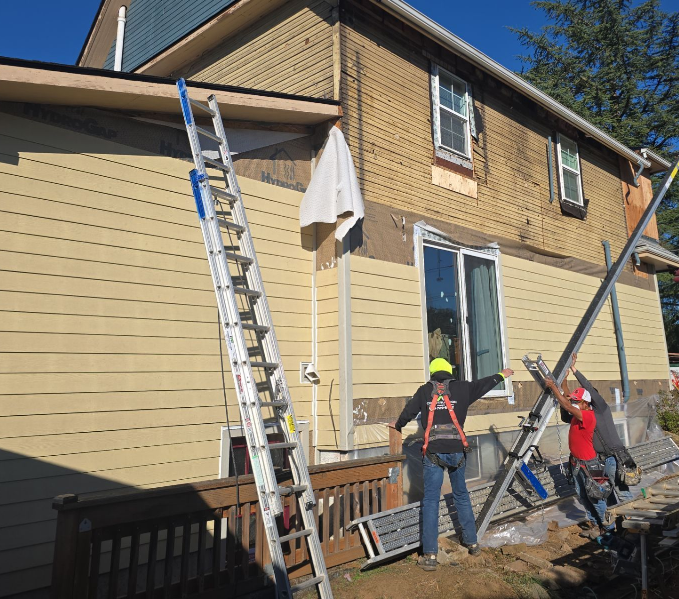 Workers on ladders painting the exterior of a house on a sunny day