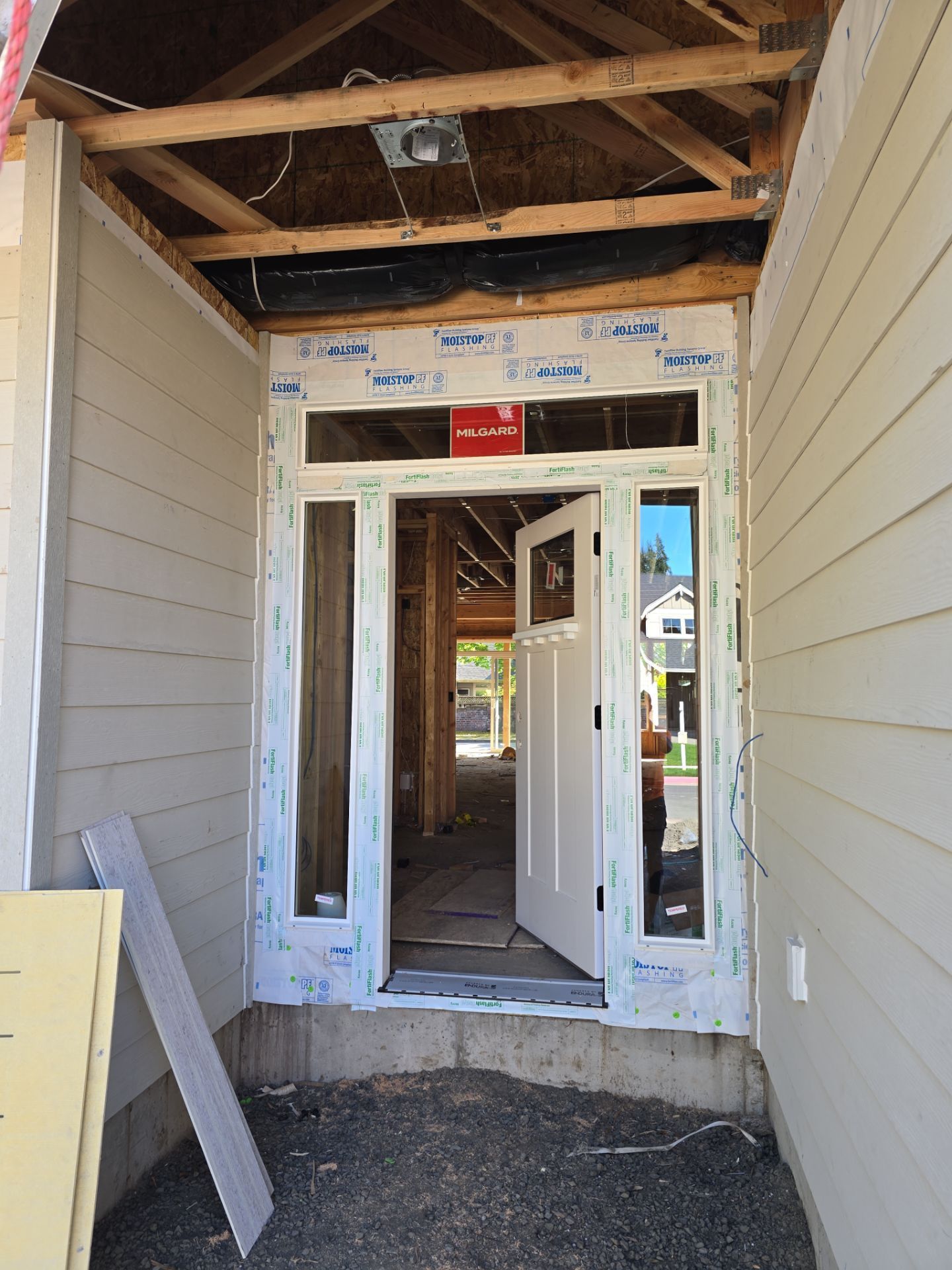 Construction doorway with exposed framing and white siding in a narrow exterior passageway