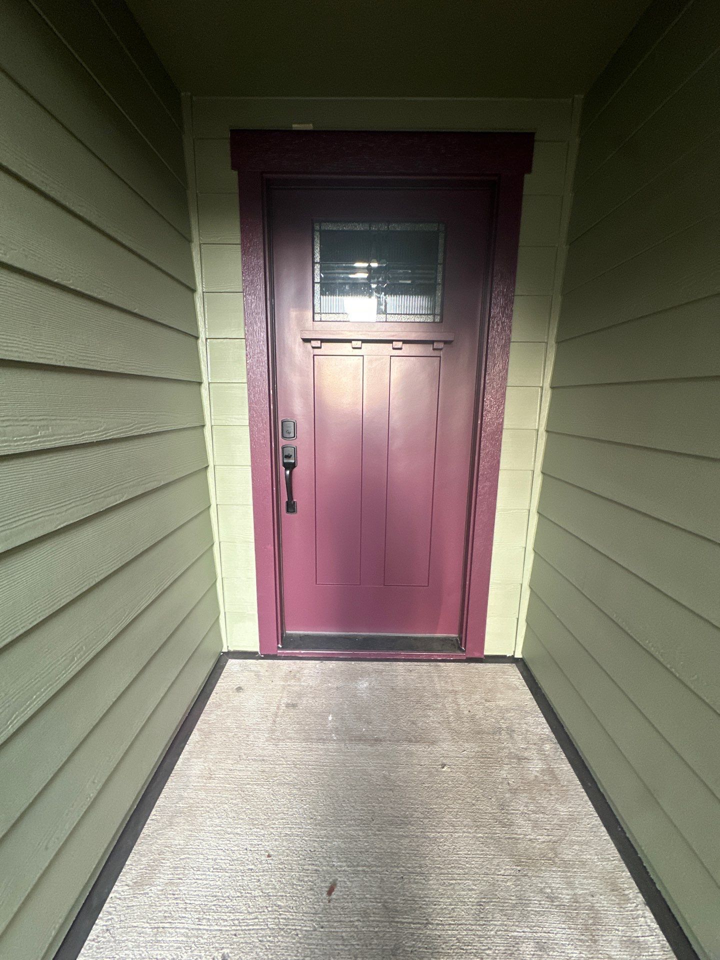 Mauve front door with small window at the end of a narrow concrete walkway between green siding walls