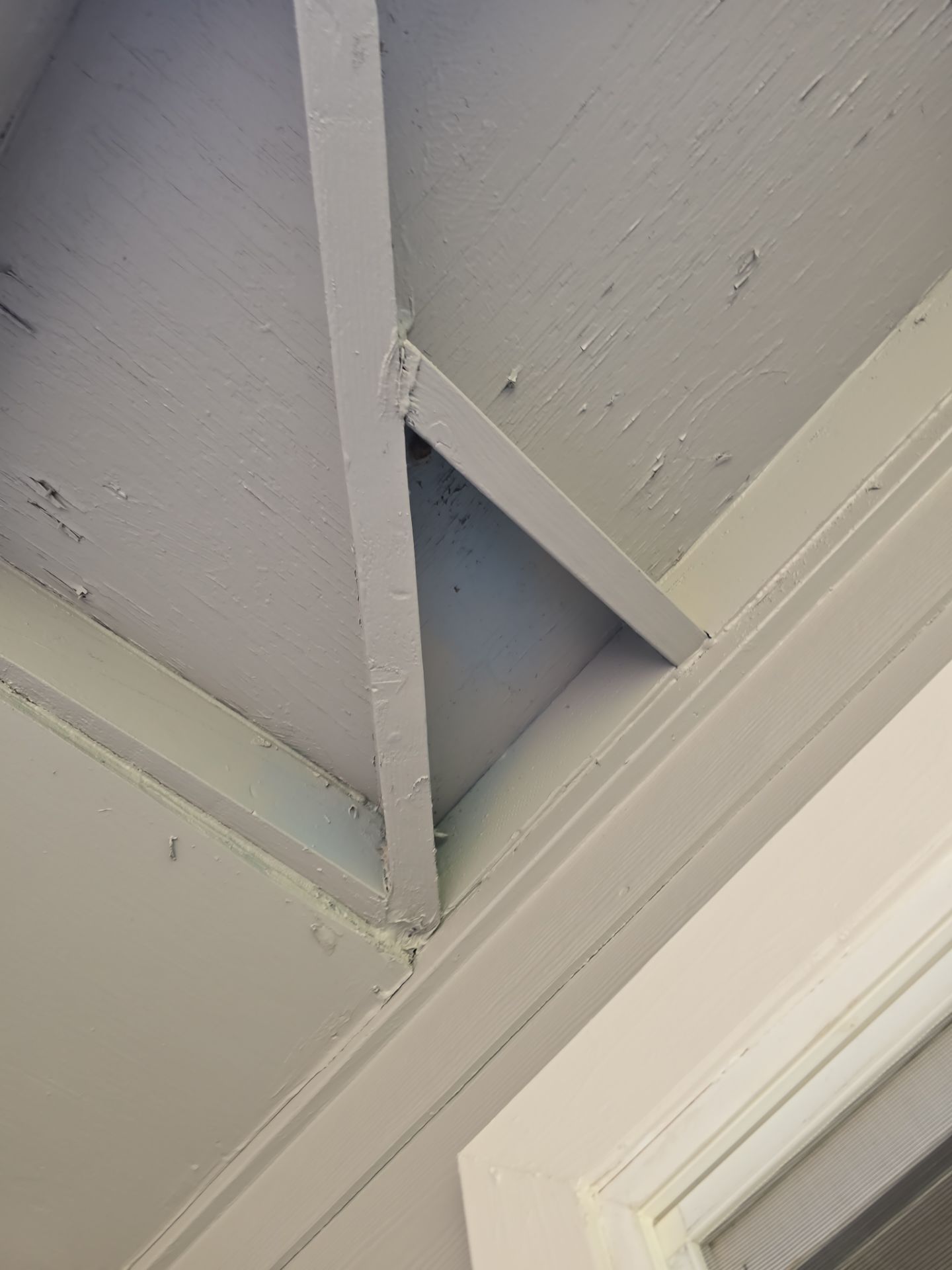 White-painted ceiling beams and molding in a corner with a small gap showing blue behind them.