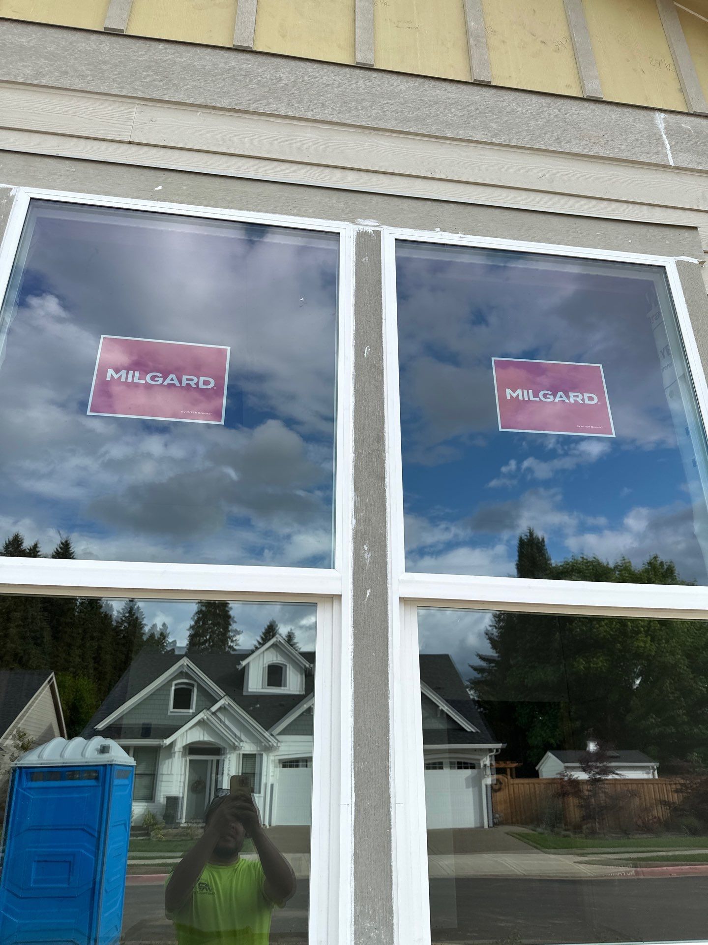 Storefront window with red signs, reflected houses, and a blue portable toilet outside