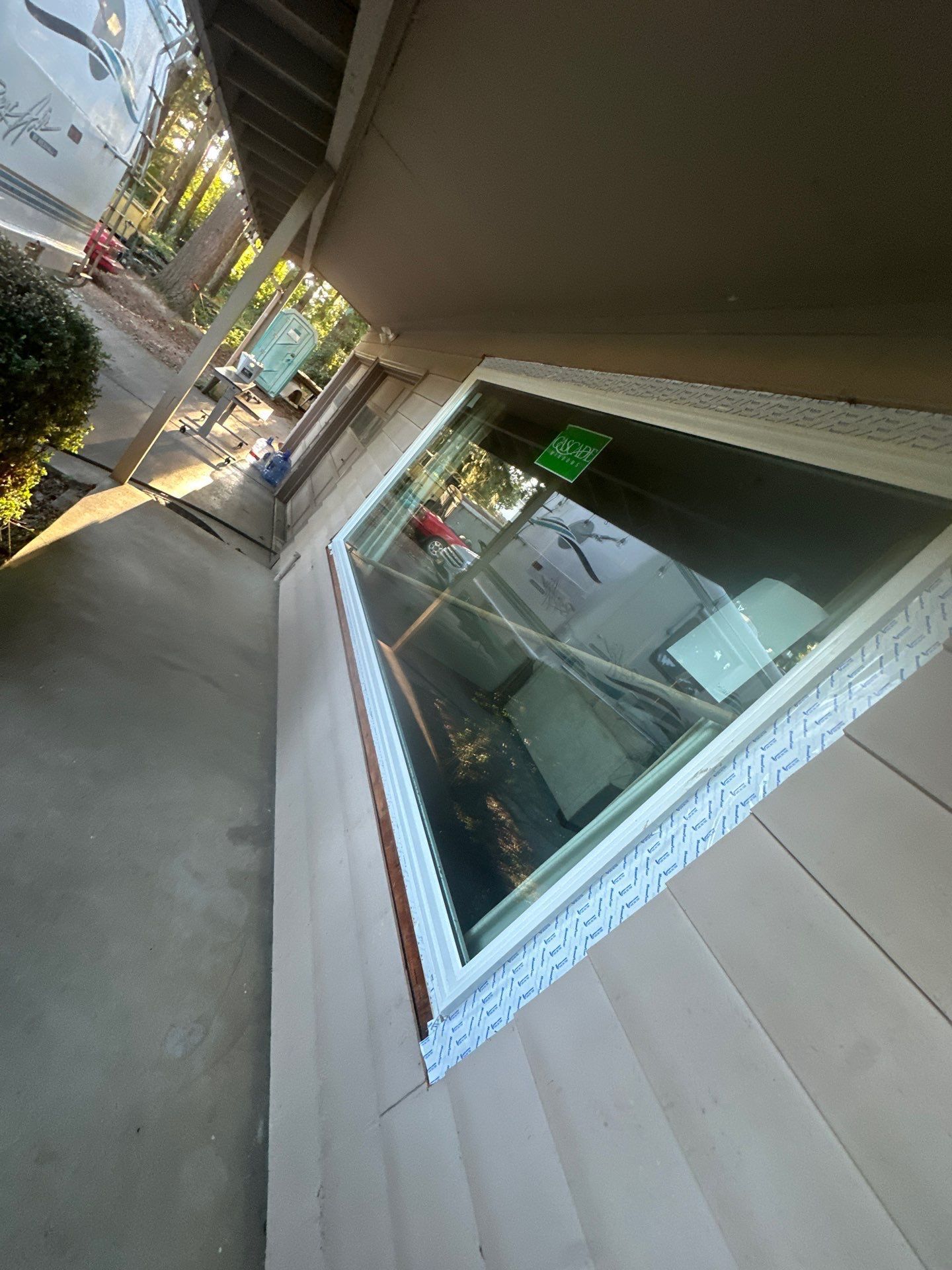 Tilted view of a storefront window and beige siding beside a narrow outdoor walkway