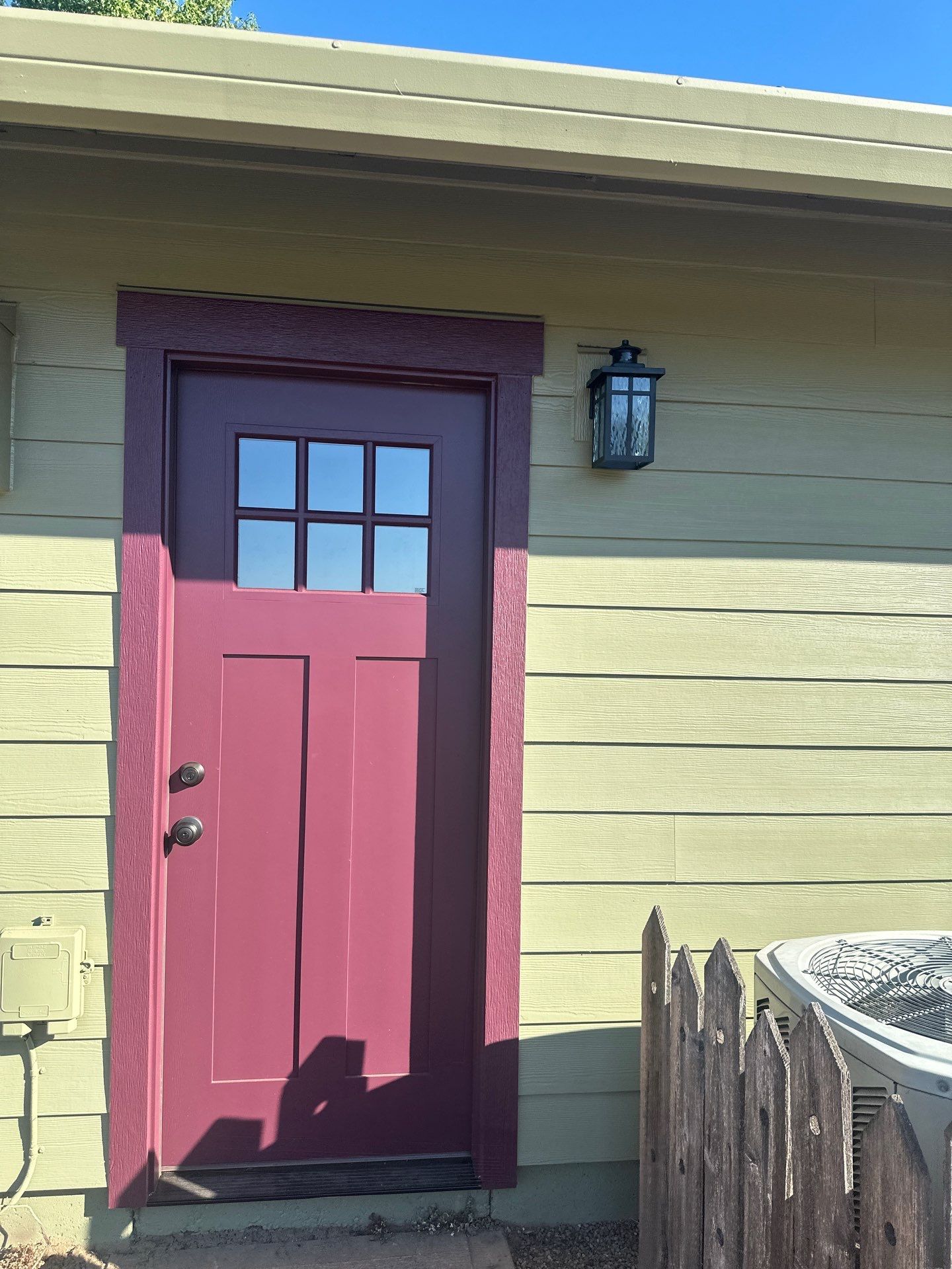 Red front door with four windows beside a wall-mounted lantern on a house exterior.