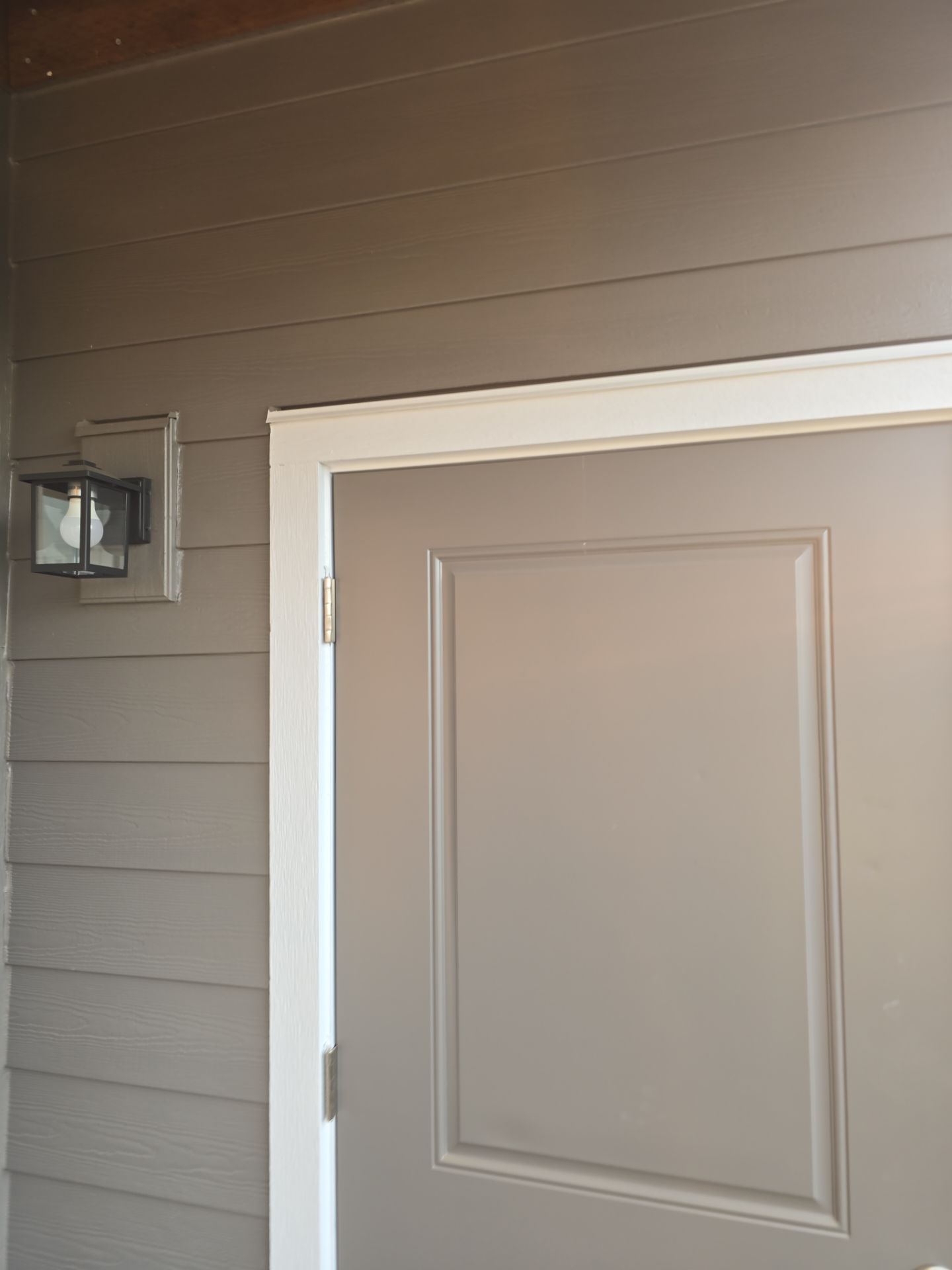 Exterior white door beside a wall-mounted porch light on gray siding