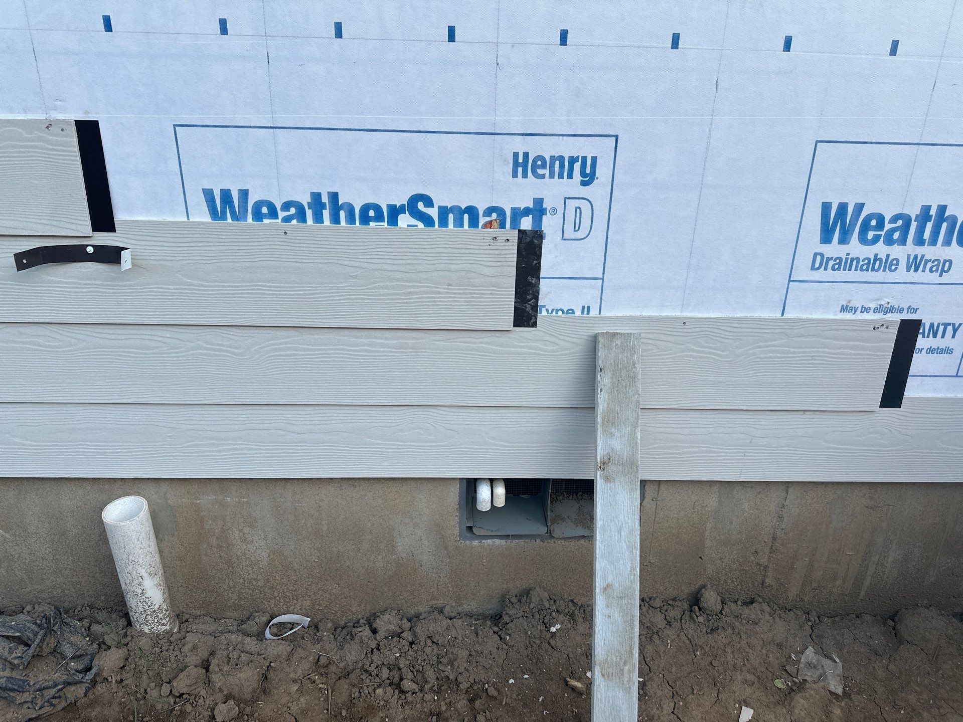 Partially built wooden deck framing against house wall with insulation and foundation visible