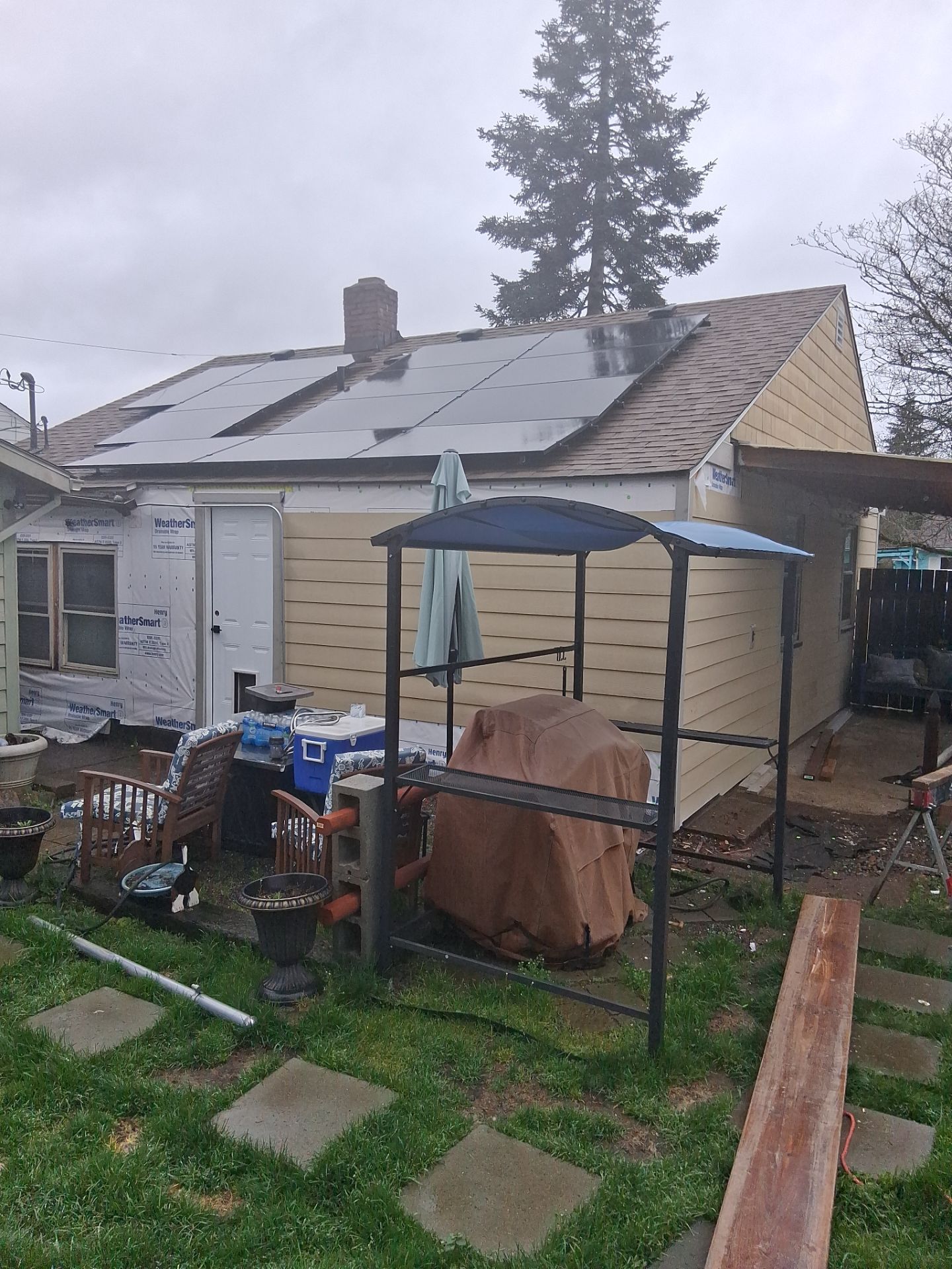 Damaged house with torn roof and scattered debris in a cluttered backyard