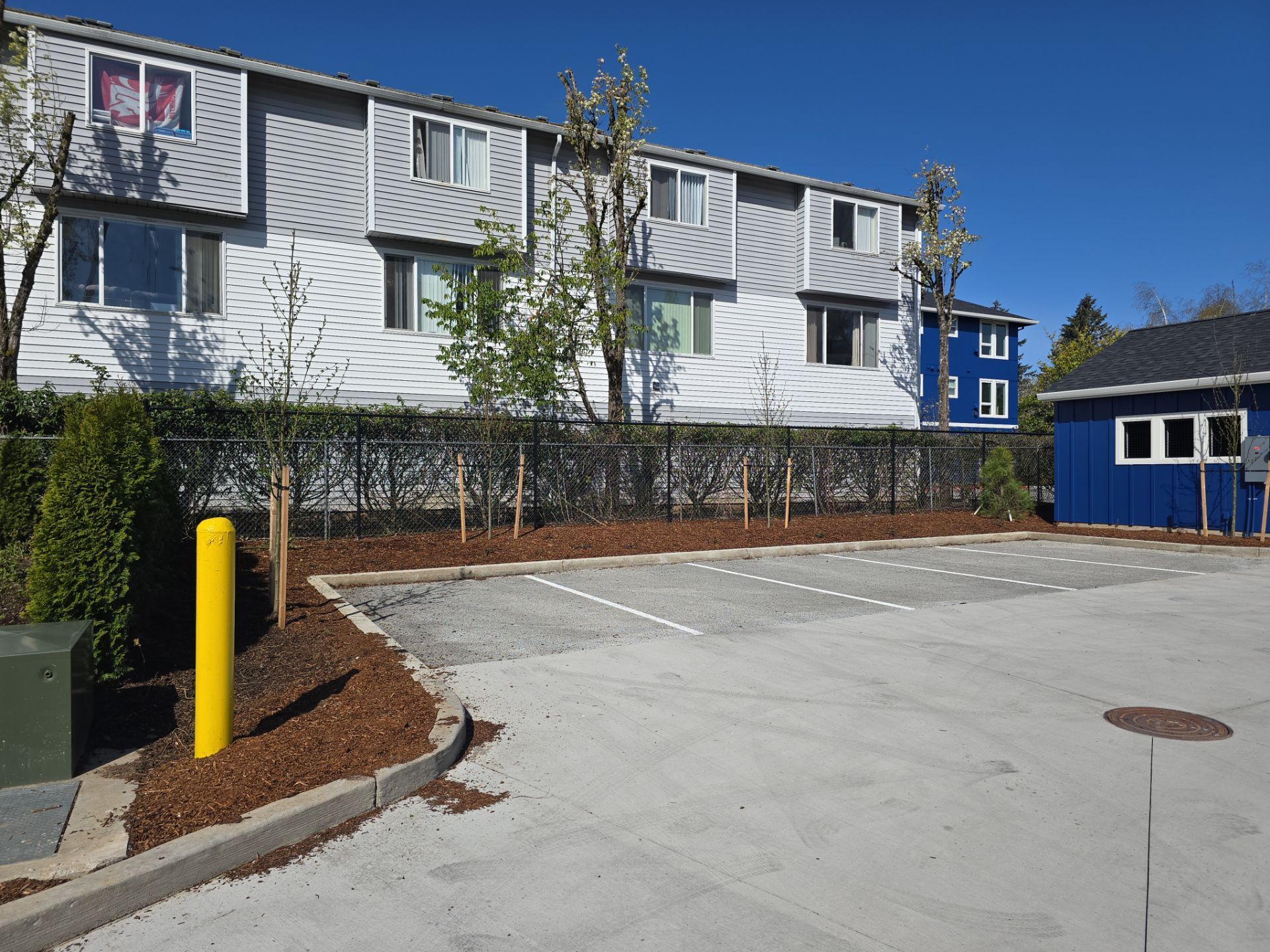 Apartment building with white siding, blue accents, and a paved parking area under a clear sky