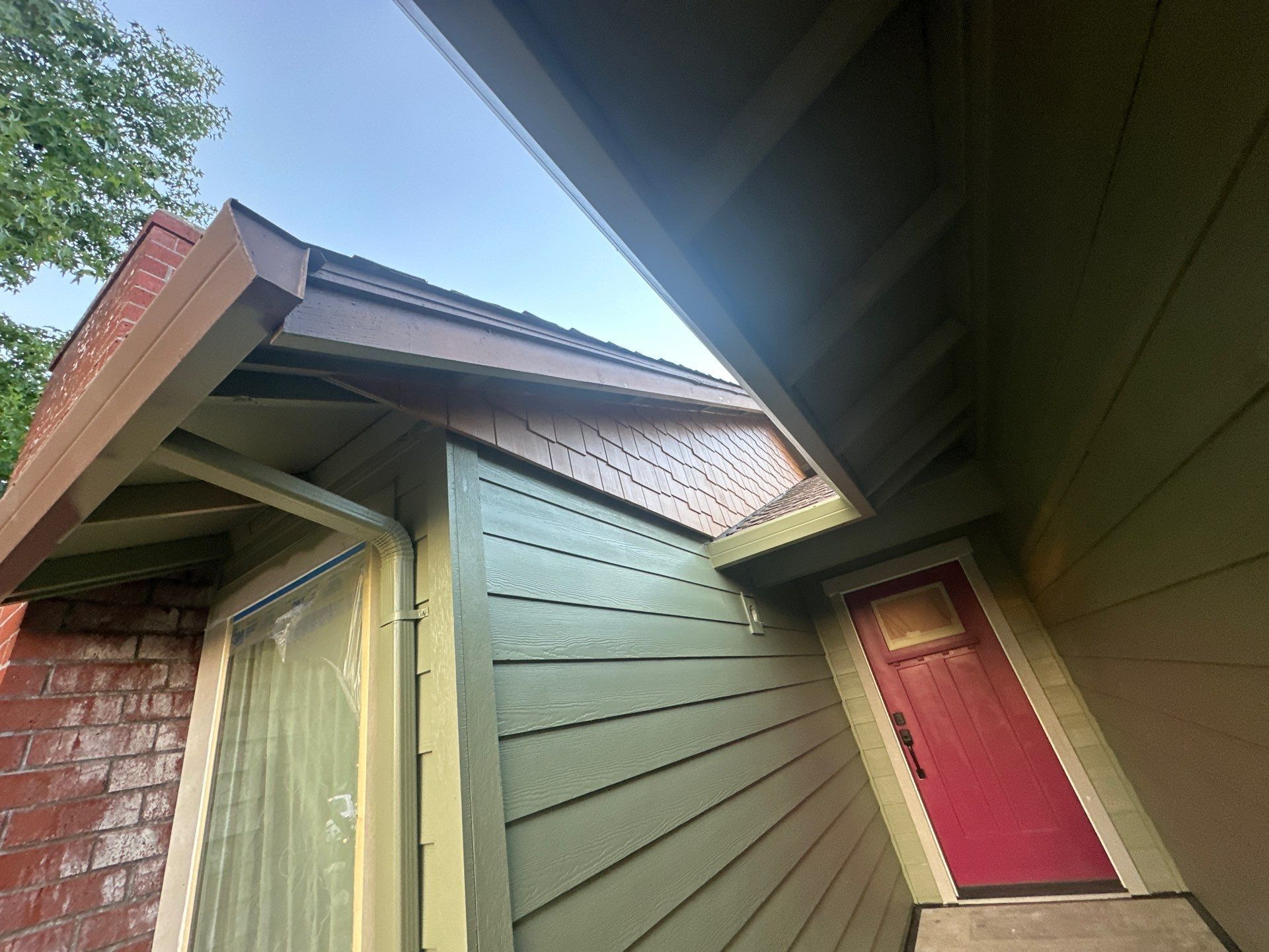 Exterior view of angled house eaves with green siding, red brick, and a pink door under a cloudy sky