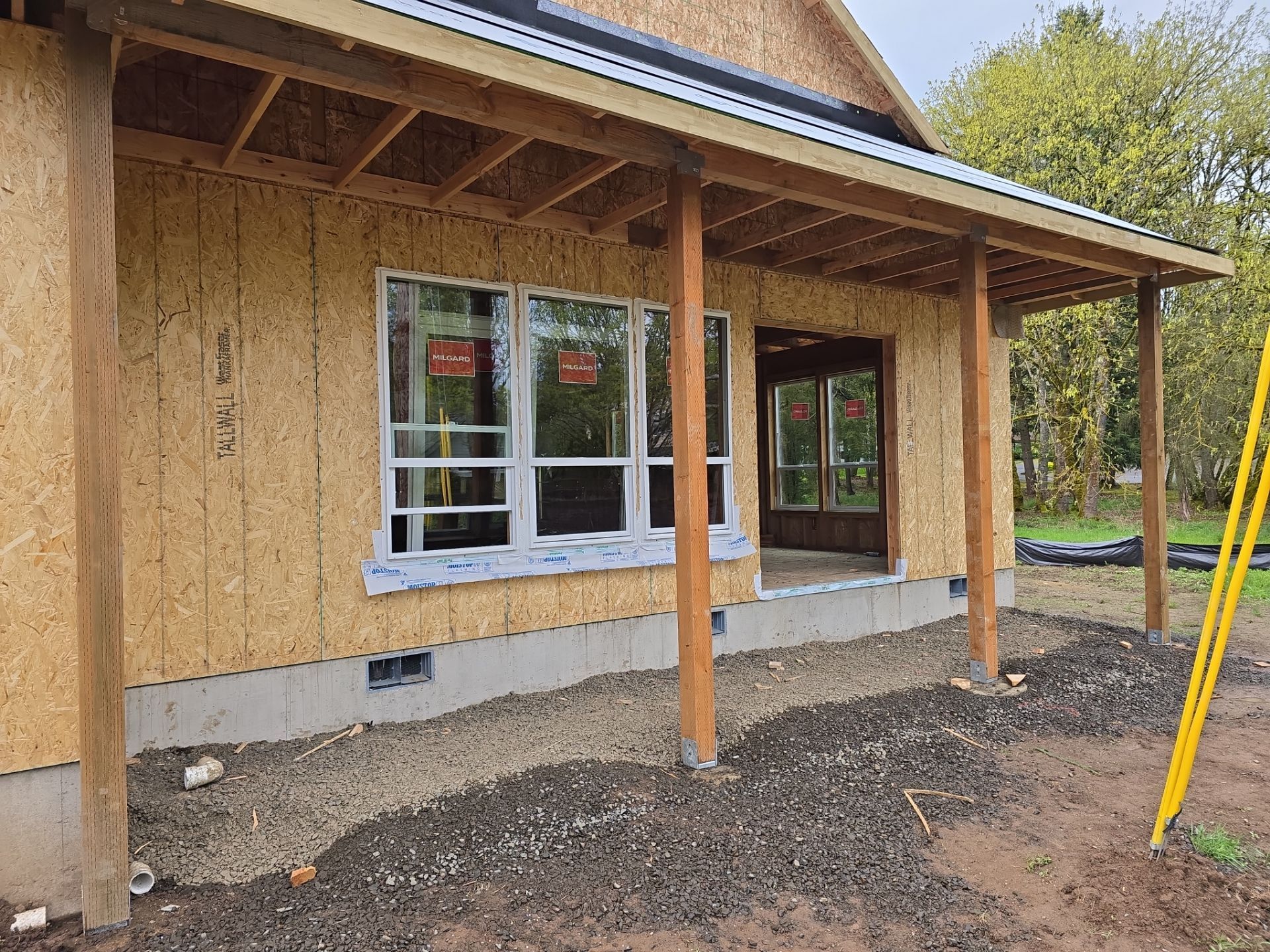 Partially finished wooden house exterior with porch posts, window, and dirt foundation area