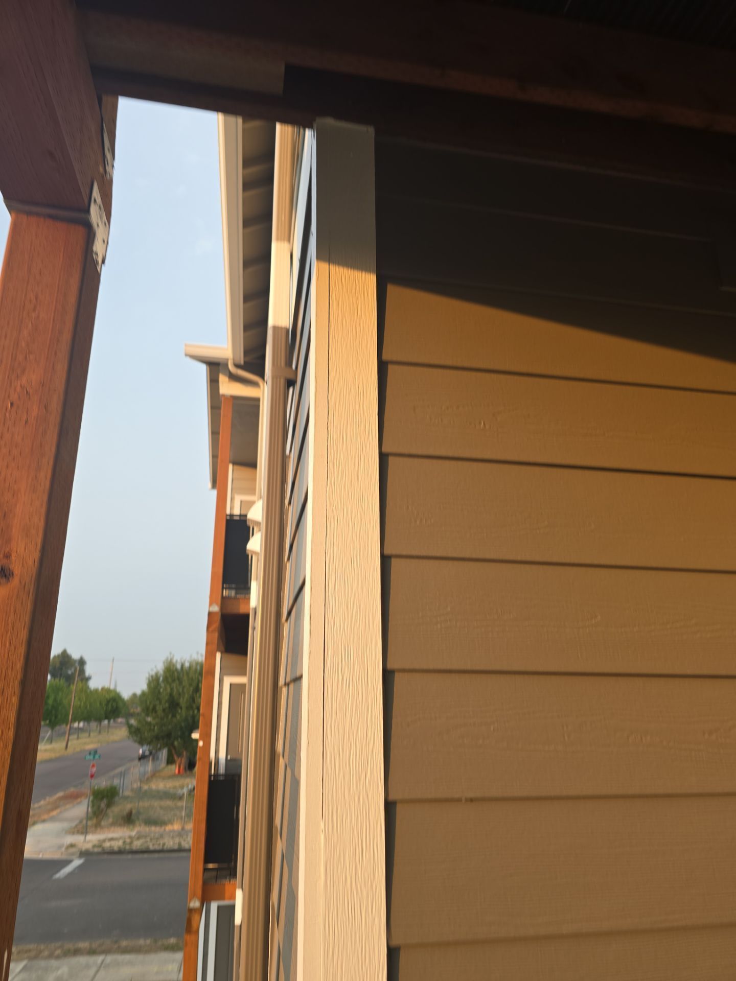 Exterior of a building with tan siding and wooden beams, viewed from a narrow side walkway.
