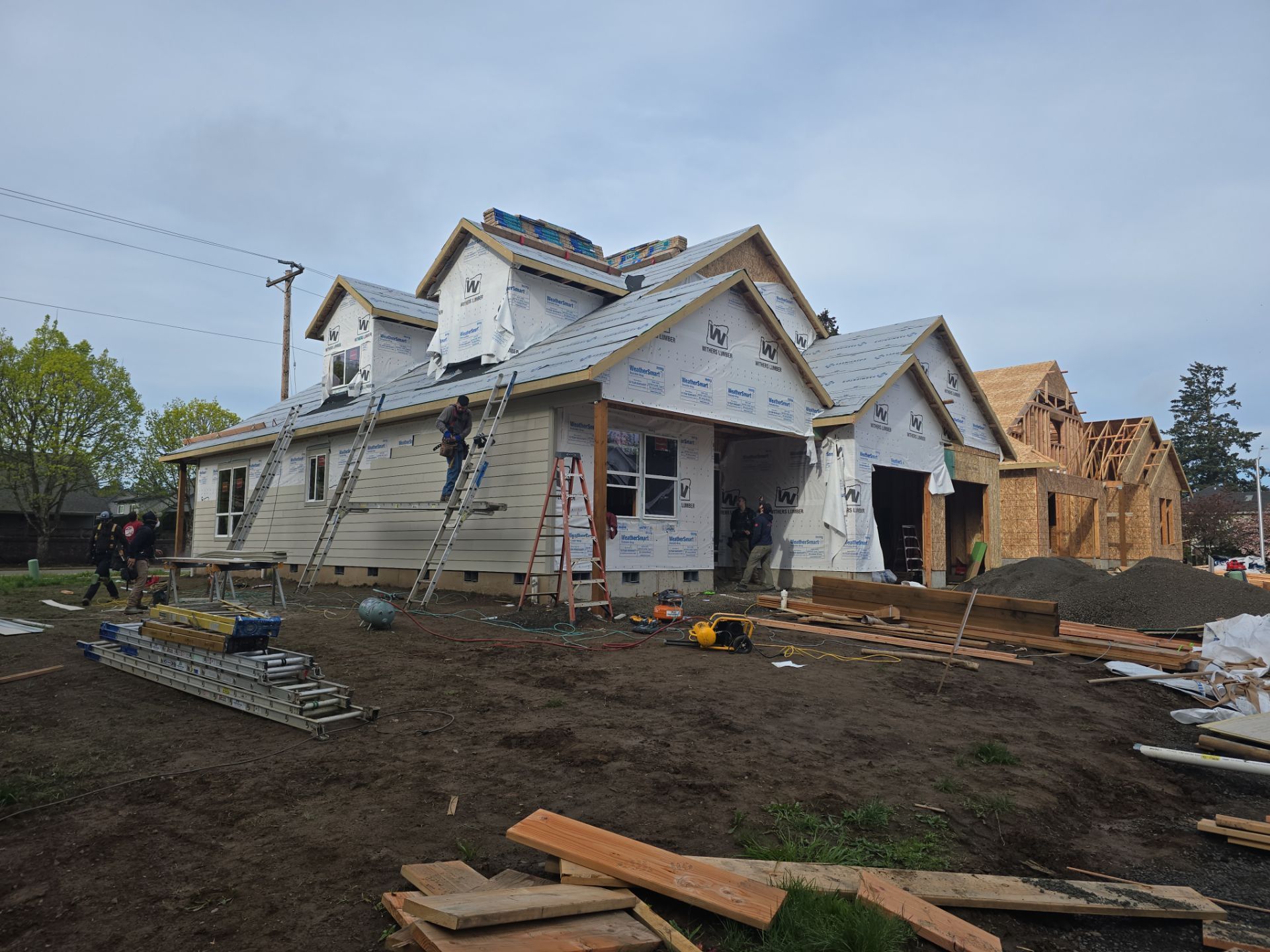 Partially built house with house wrap, exposed framing, and muddy construction site under cloudy sky
