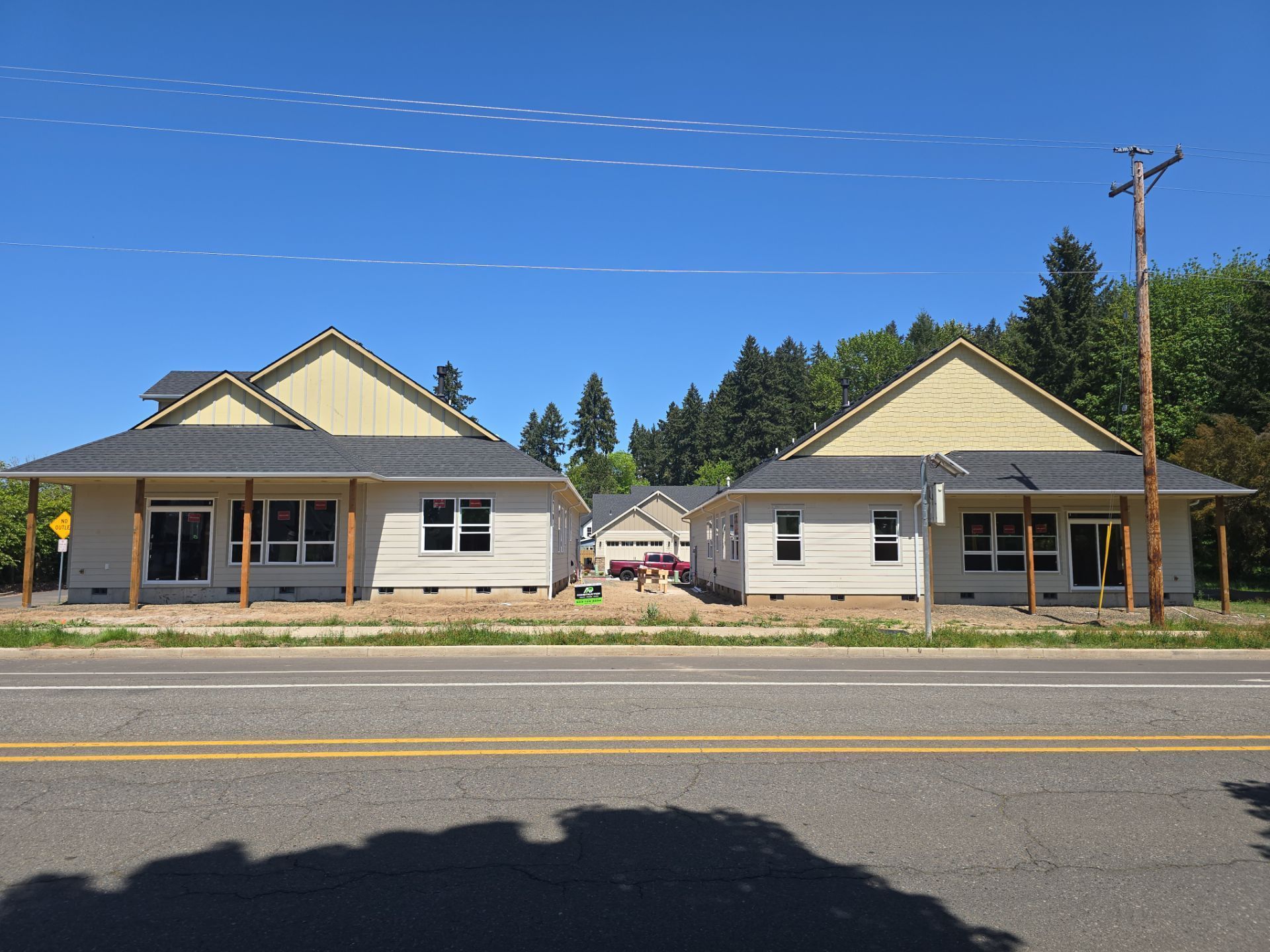 Two small gray houses with green roofs across a road under a clear blue sky