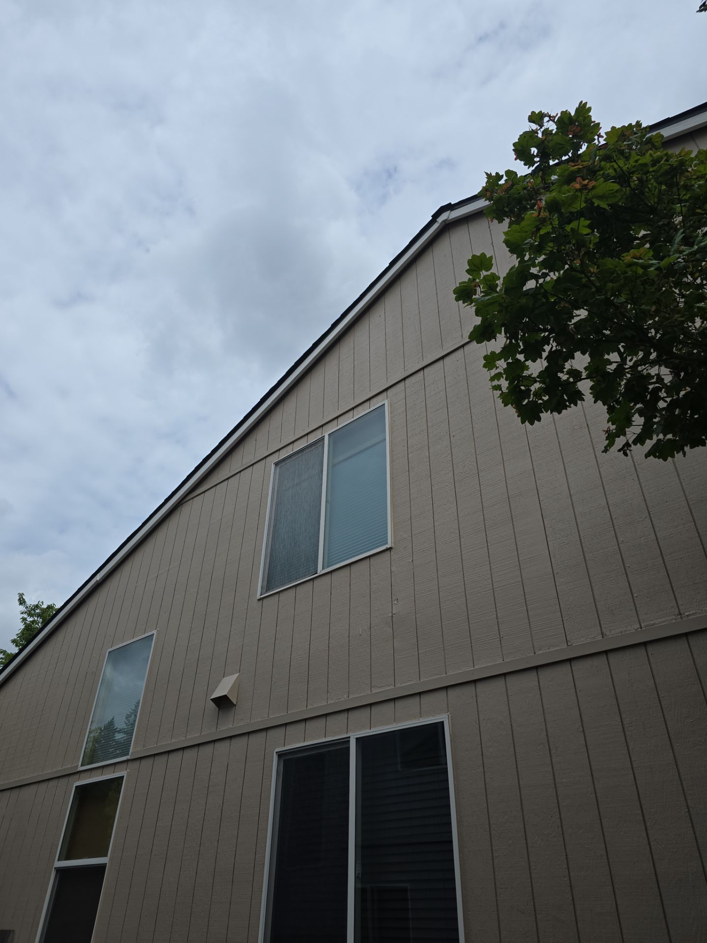 Exterior of a beige two-story house with windows, seen from below against a cloudy sky