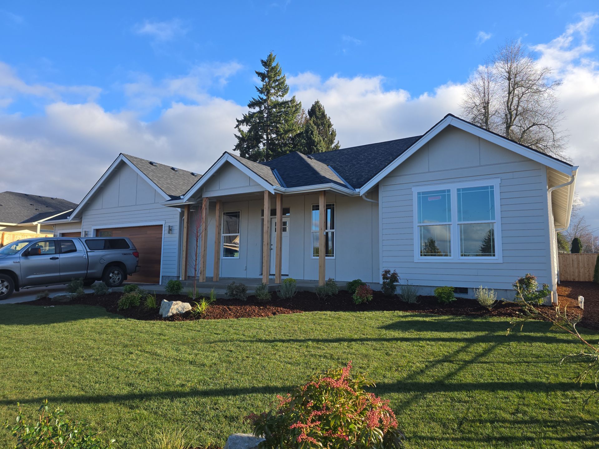 Single-story white house with a front porch, lawn, and parked pickup truck under a blue sky