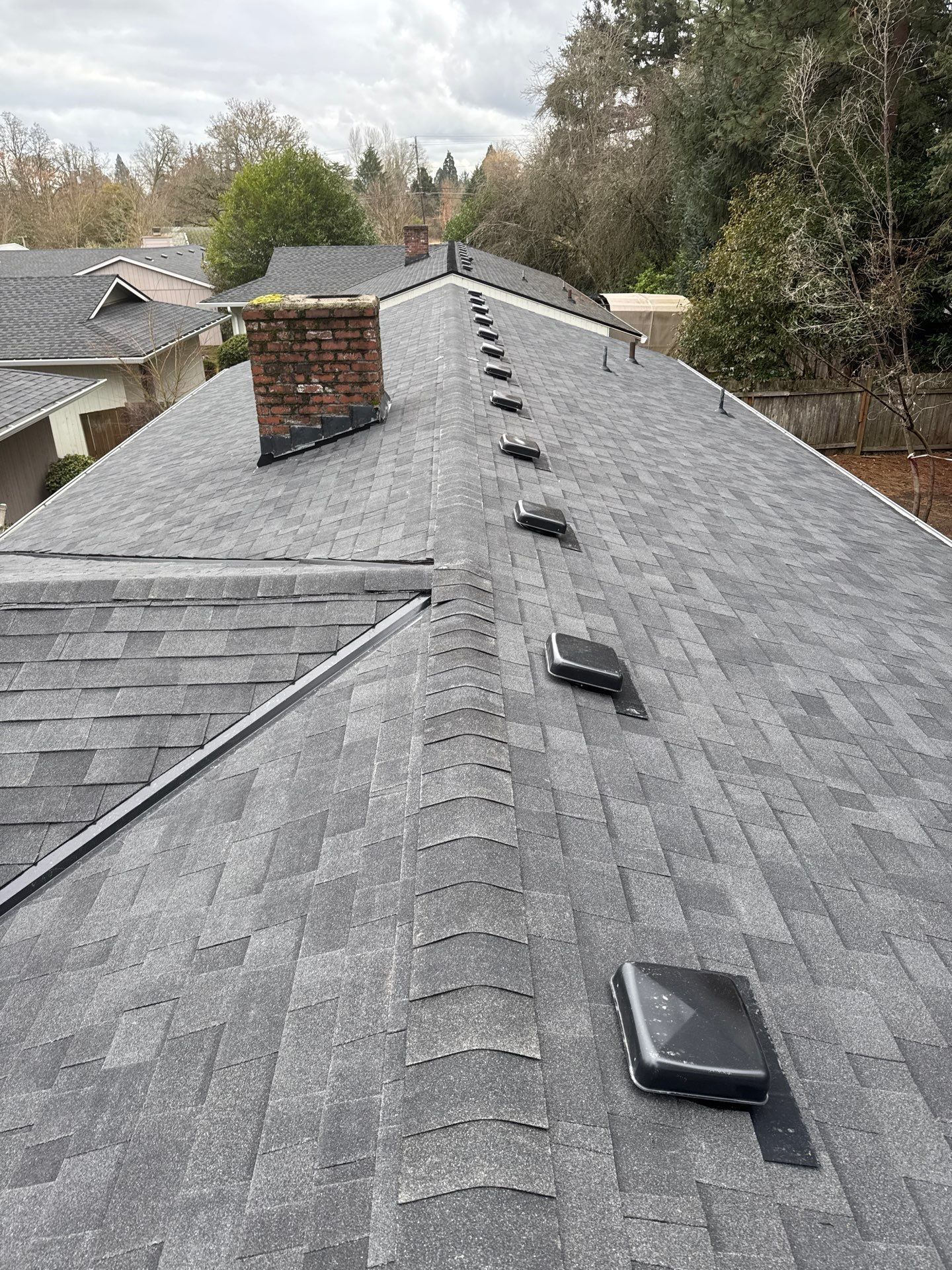 Gray shingled roof with skylights and a brick chimney, viewed from above in a suburban neighborhood