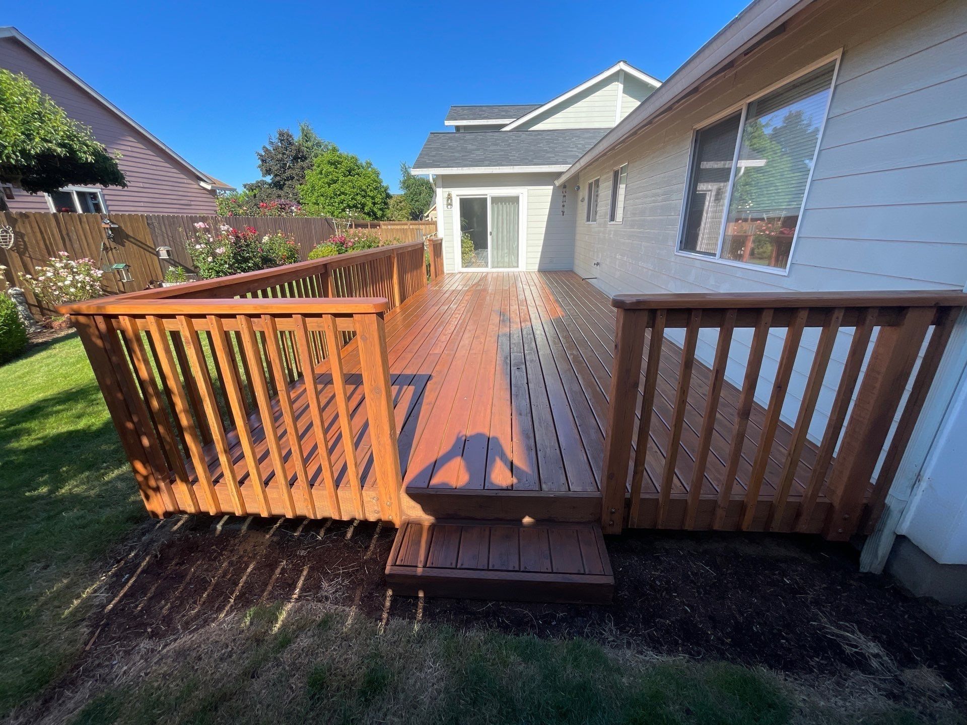 Wooden backyard deck with railings beside a white house on a sunny day