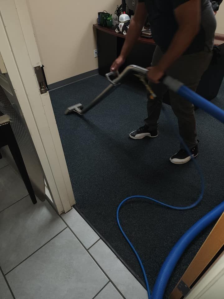 Person cleaning a dark carpet with a professional machine in an office.