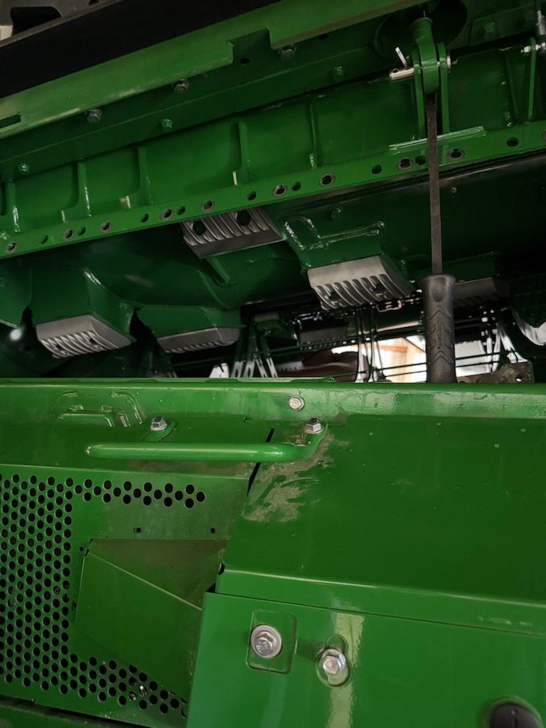A close-up view of the green mechanical interior of a John Deere agricultural machine, showing internal components.