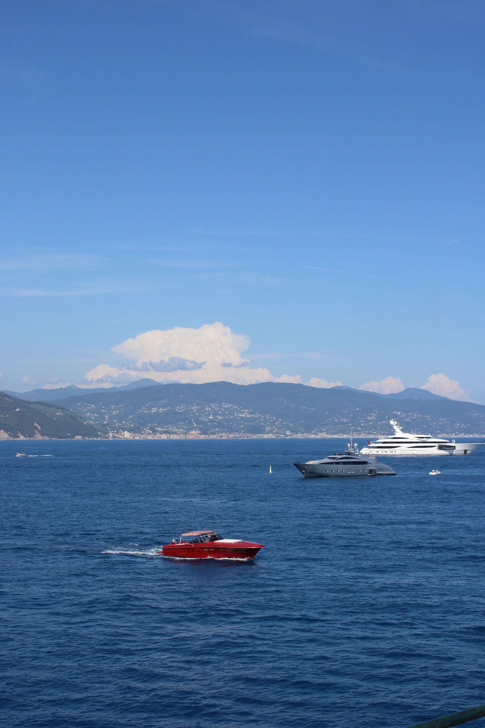 Boats on blue water with a distant shoreline and city under a clear sky