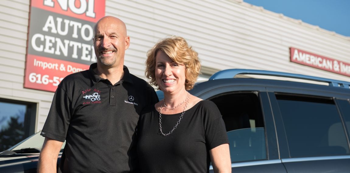 A man and woman stand outside an auto repair shop. The man wears a black shirt, the woman a black top. | Arie Nol Auto Center