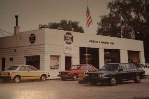 A car repair shop in the 1980s with American flag and three cars parked in front. | Arie Nol Auto Center
