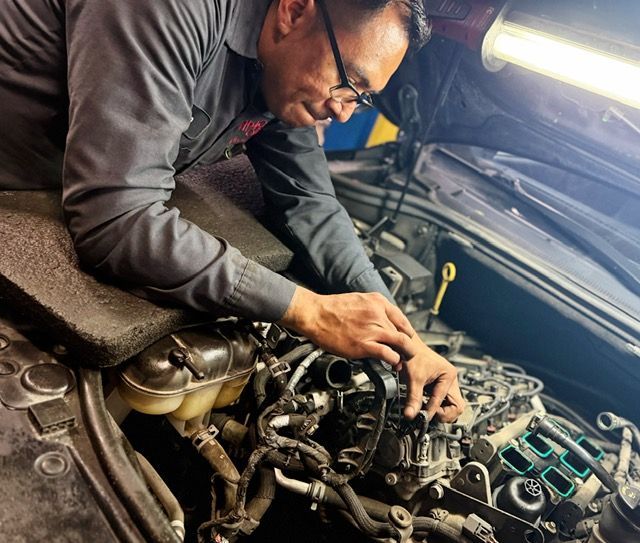 Five auto mechanics stand under a raised car, smiling. They are in a garage, wearing black shirts.| Arie Nol Auto Center