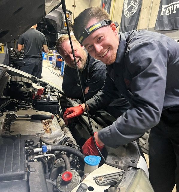 Four mechanics with arms crossed, in a garage under a lifted car. | Arie Nol Auto Center