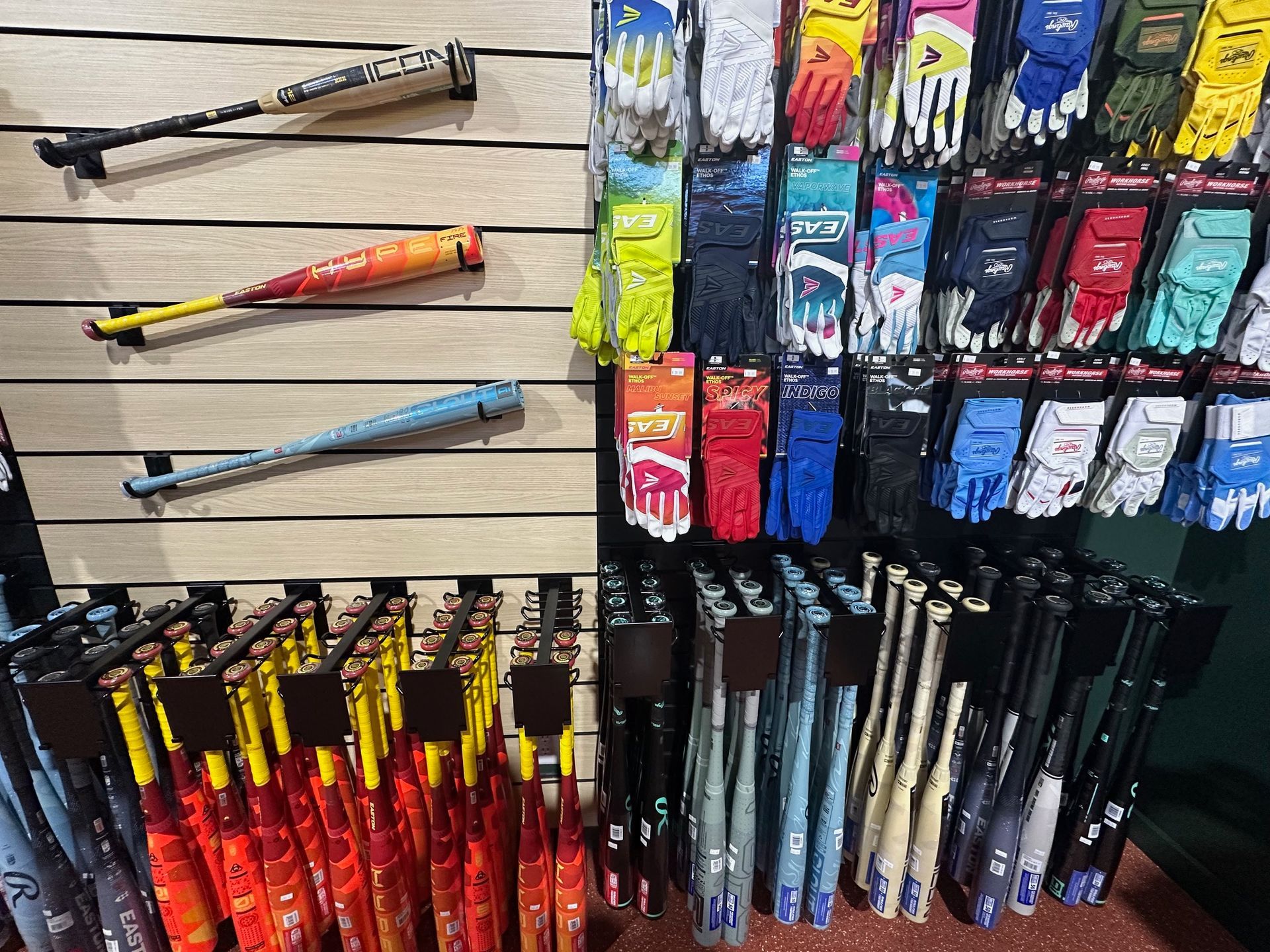 Colorful baseball bats and rackets displayed on a store wall and in a floor bin
