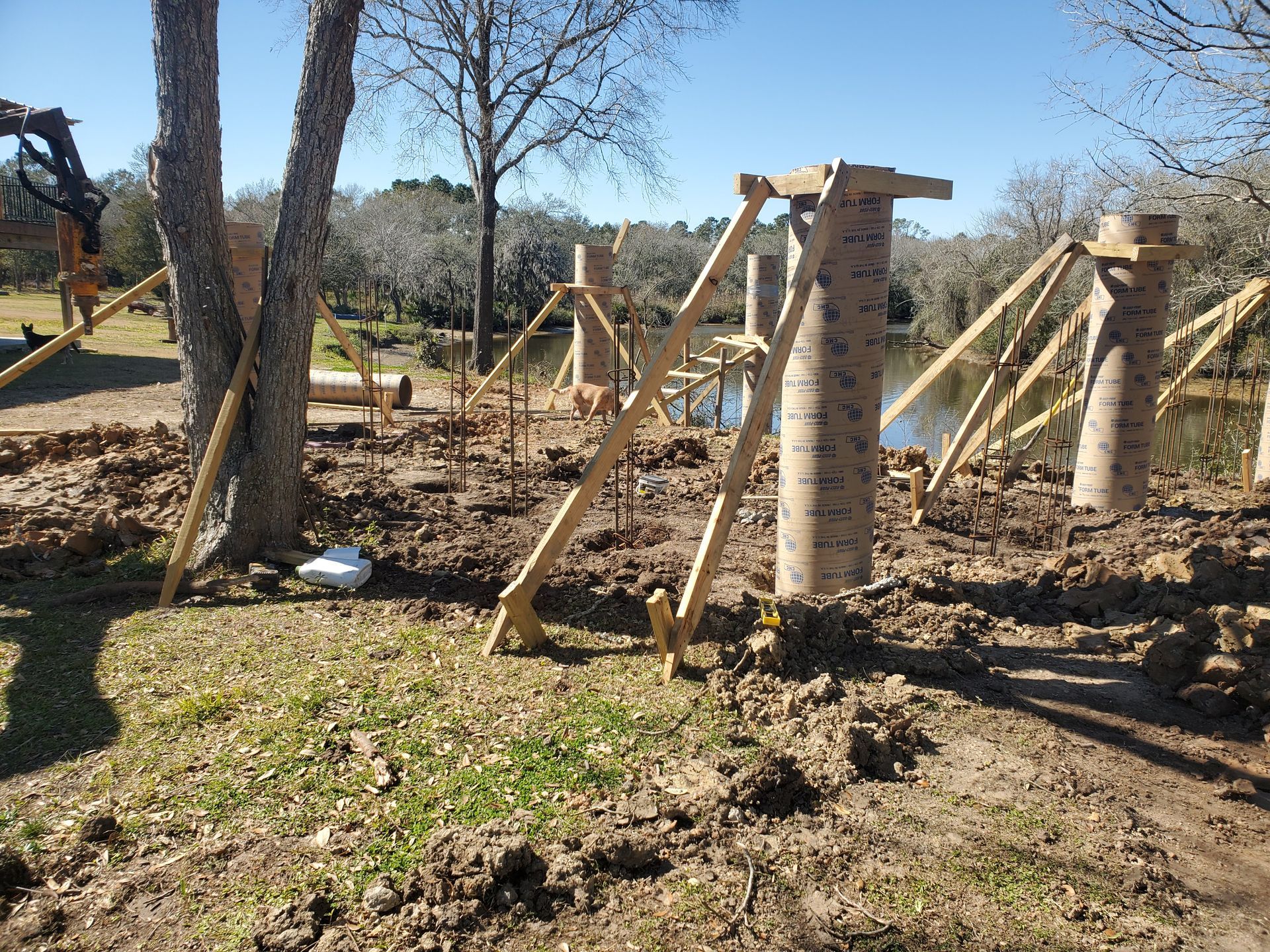 Construction site with brick columns being supported by wooden braces, near a body of water.