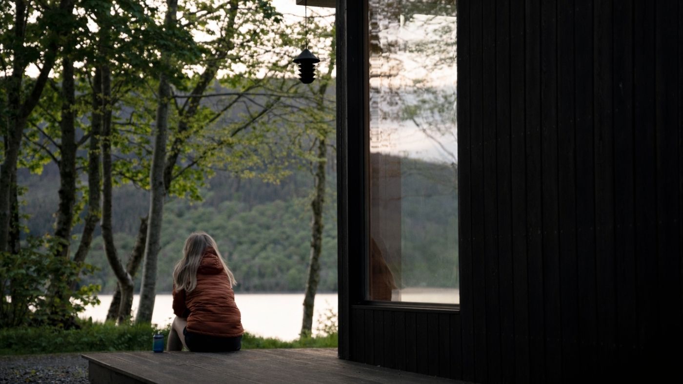 Guest seated by a window overlooking the loch from a secluded Scottish cabin