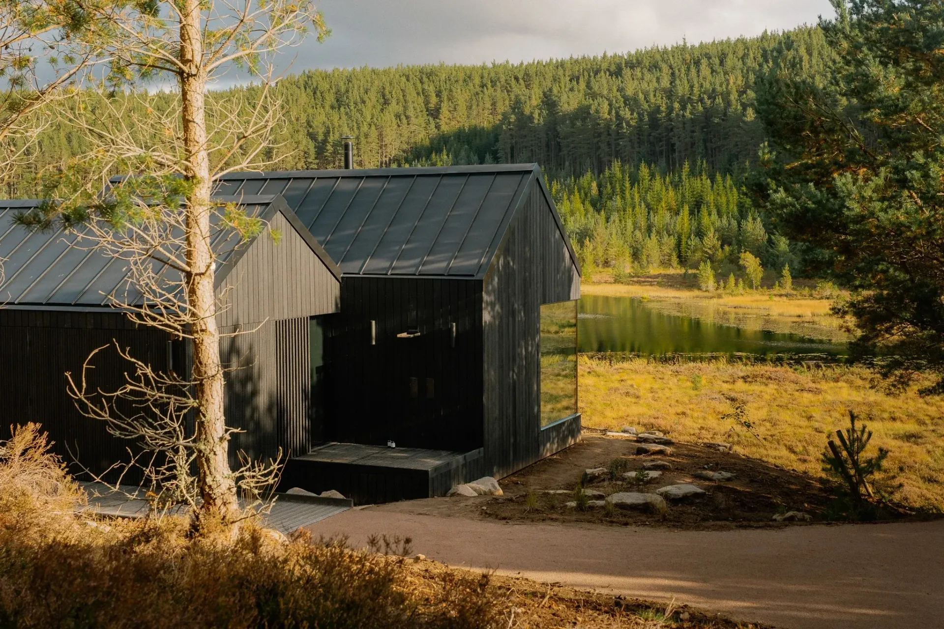 Moya Kabn, a secluded luxury cabin in the Cairngorms, with black timber cladding overlooking a peaceful forest lochan.