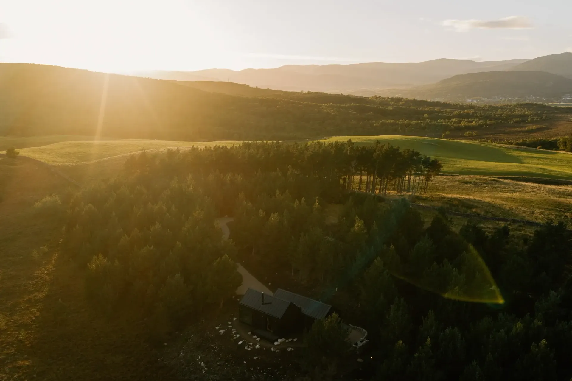 Golden sunset over the Cairngorms landscape, with Moya Kabn nestled among pine trees beneath the rolling Highland hills.