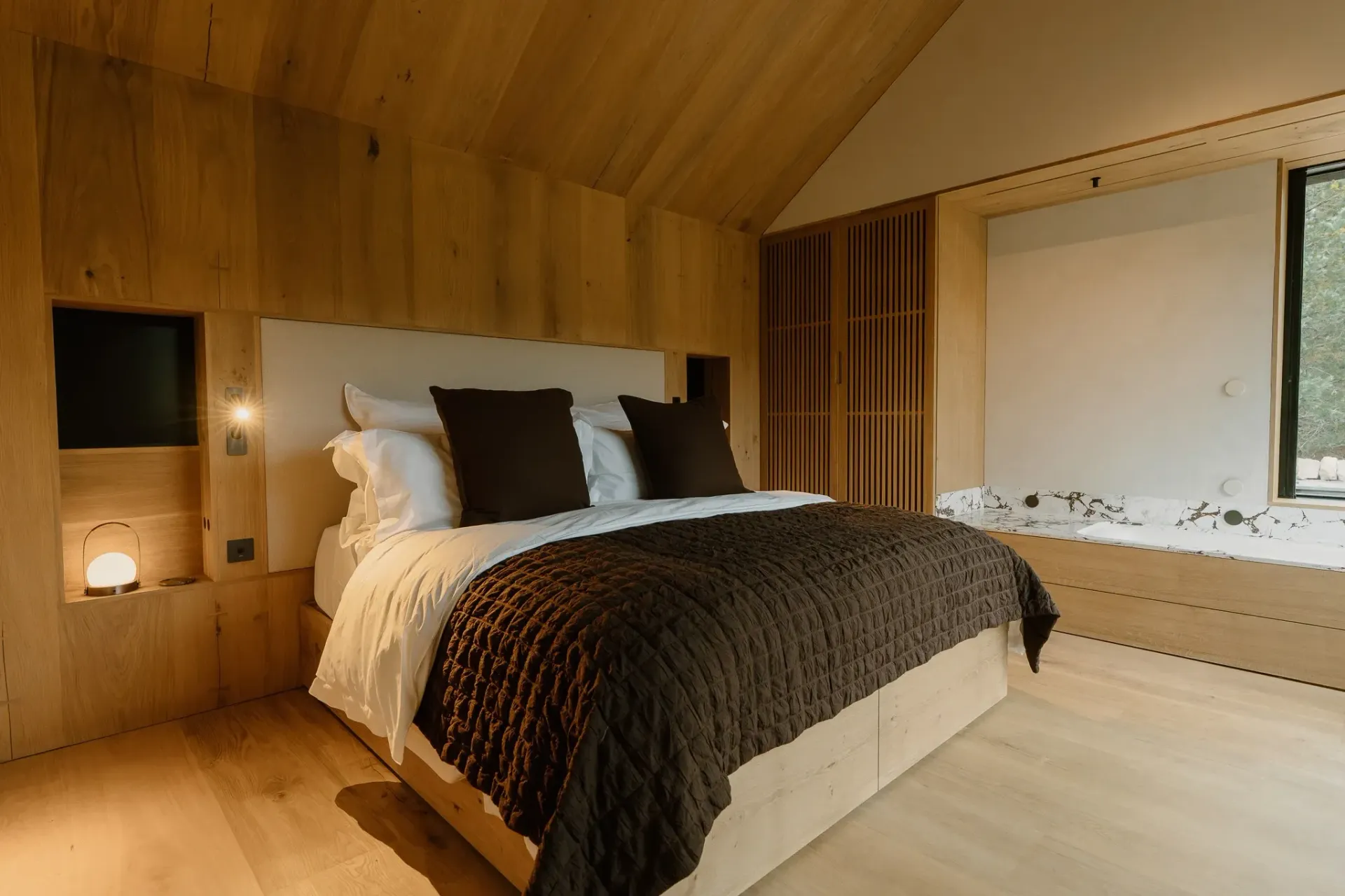 Luxury bedroom suite at Moya Kabn, featuring a king-size bed, natural oak interiors and a marble bath beside the window.