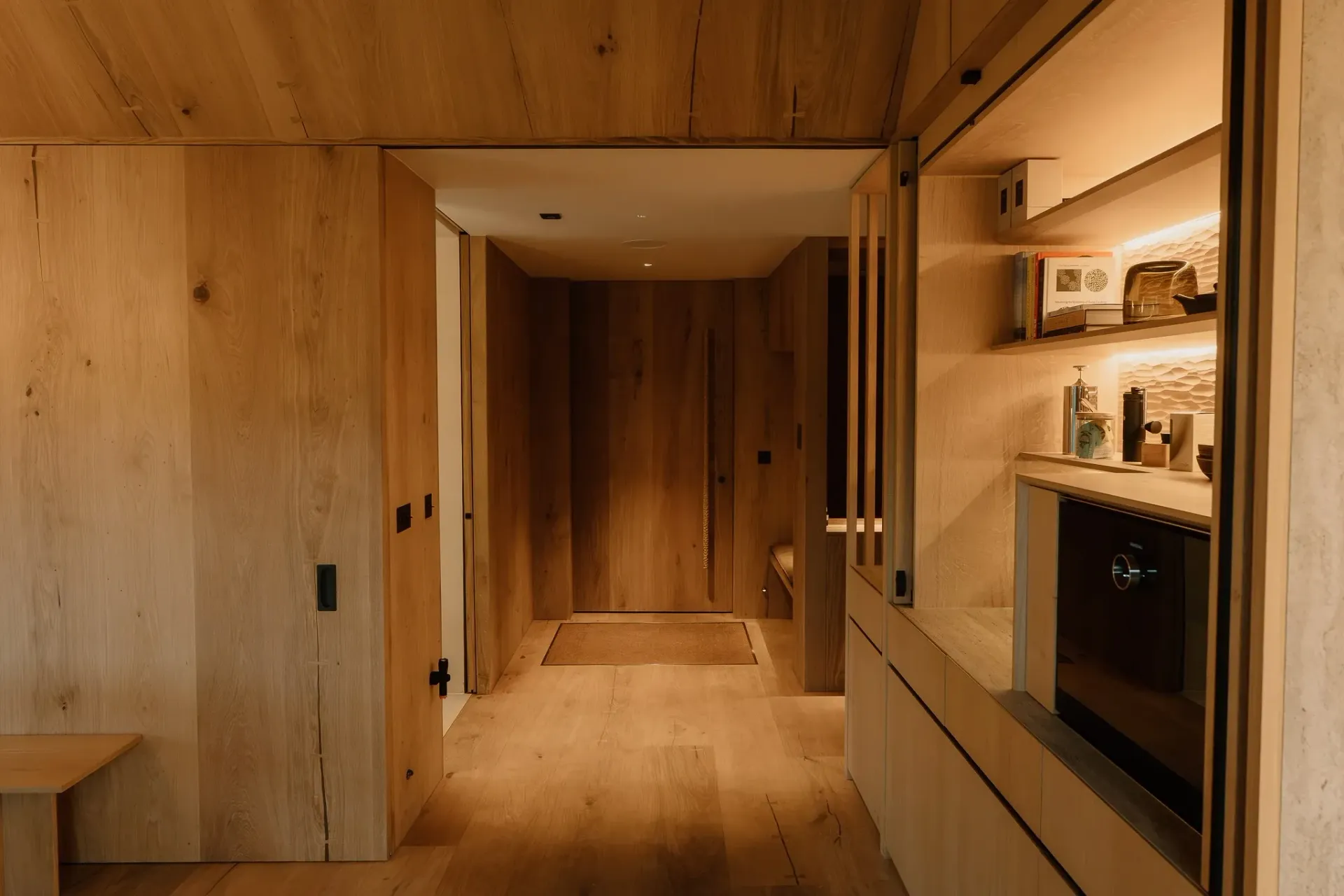 Oak-lined hallway at Moya Kabn with a bespoke minibar, illuminated shelving and cabinetry