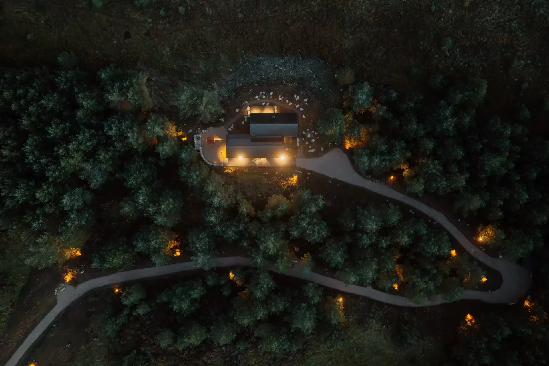 Overhead night view of Moya Kabn illuminated among pine trees, with a winding, softly lit path
