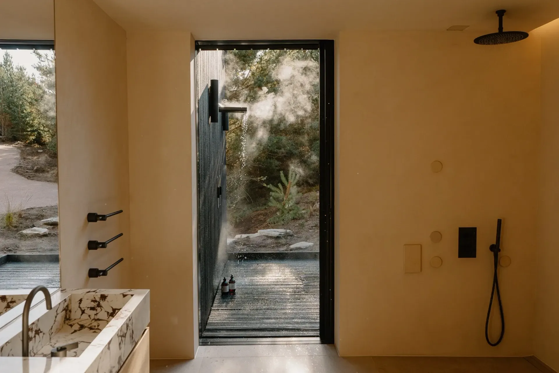 Moya Kabn bathroom with rainfall shower, marble sink and glass door to the outdoor shower