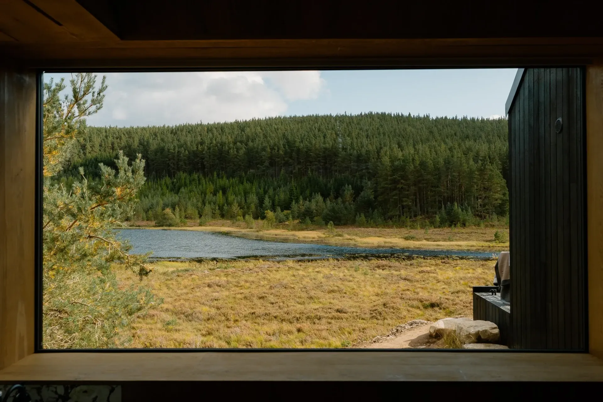 Large picture window at Moya Kabn framing the lochan and surrounding Cairngorms pine forest