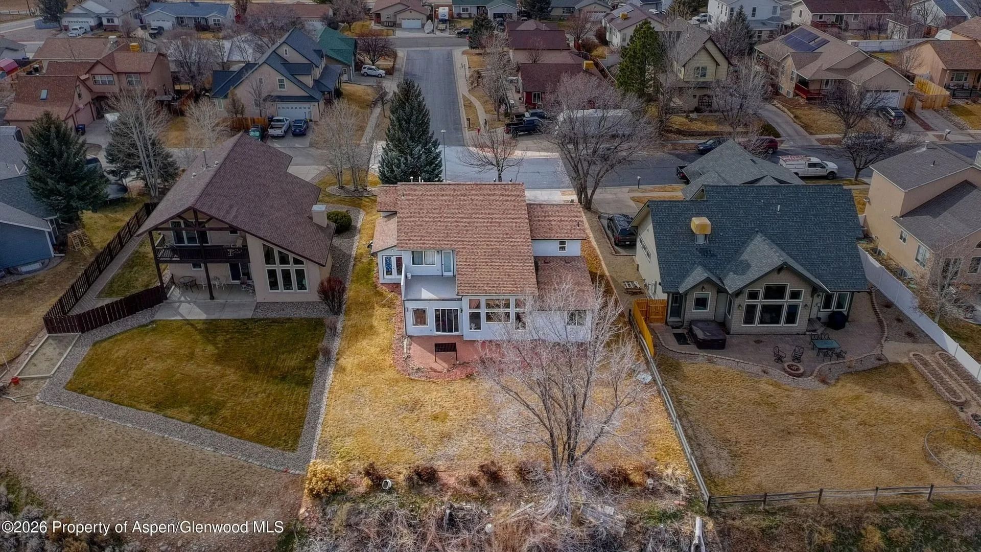 Aerial view of three suburban houses with autumn trees and yards in a neighborhood.